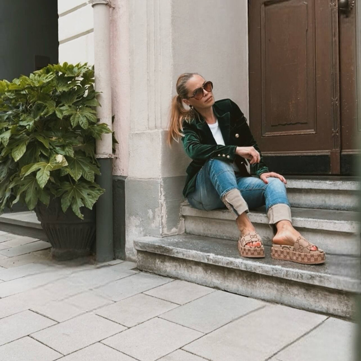 Model sitzt leicht gebeugt im CASAPARI® Samtblazer in Tannengrün. Weicher Samt, goldene Knöpfe am Ärmel. Stilvoll und Edel.