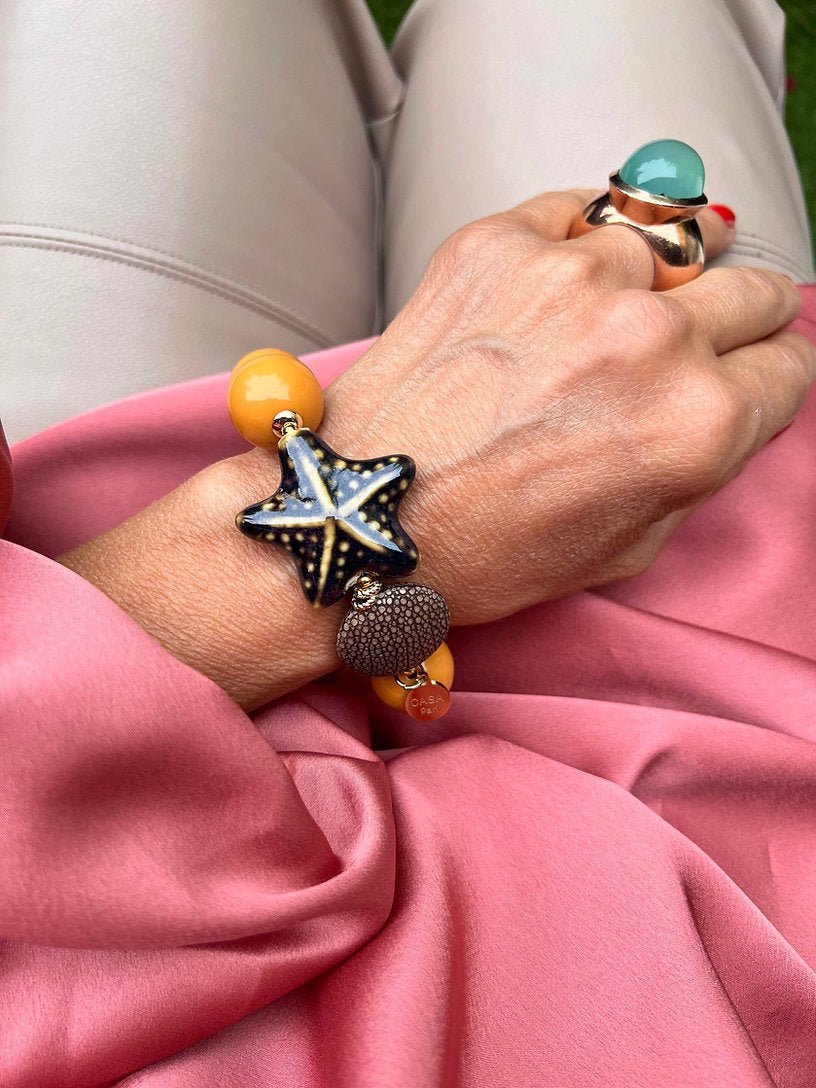 Handgelenk mit gelben Armband aus großen Perlen, verziert mit einem braunen Seestern und einem runder Perle.