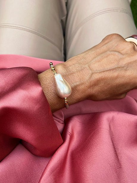 Nahaufnahme einer Hand mit Armband. Rosa mit großer Barockperle und goldfarbenen Details.