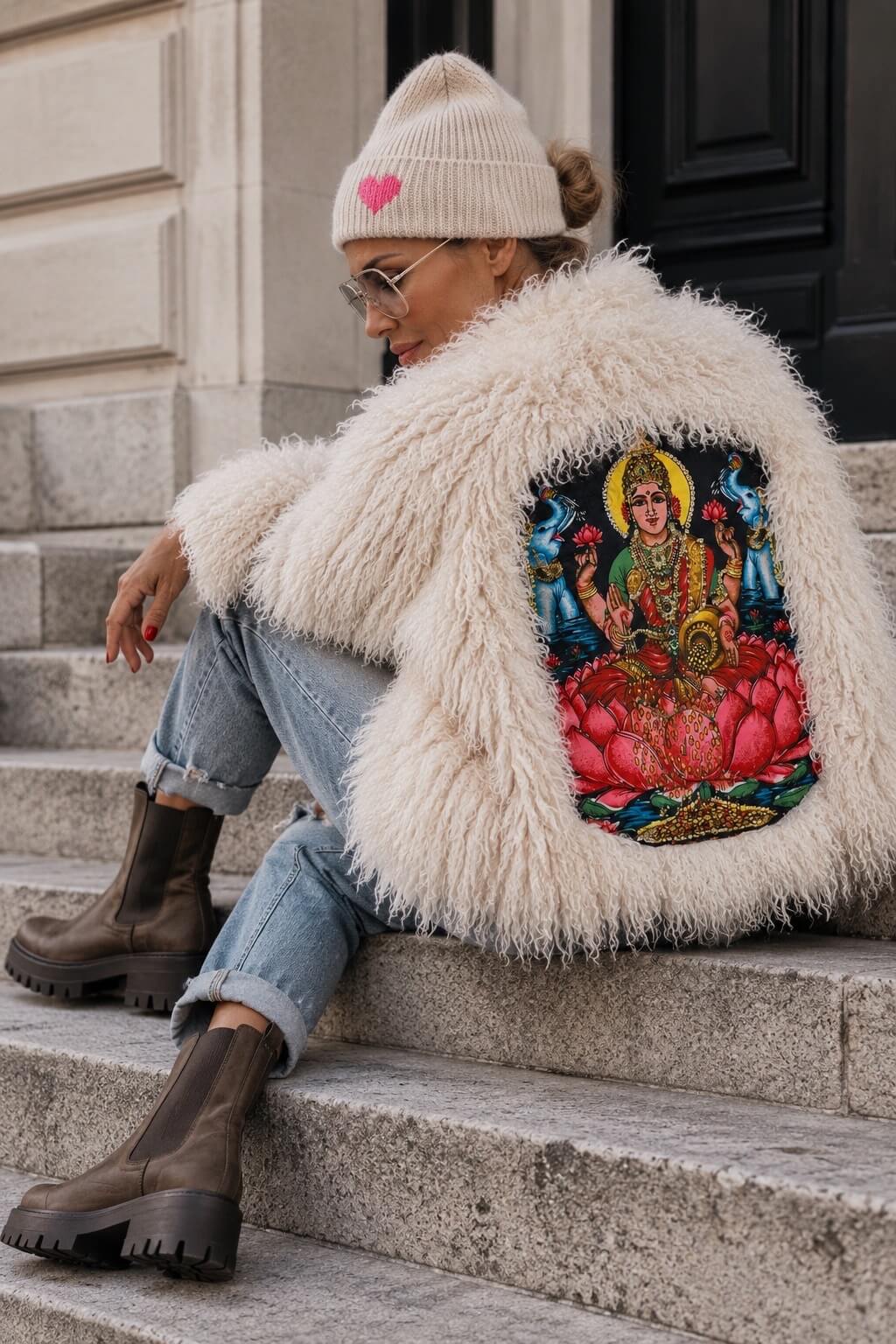 Rückansicht der cremefarbenen CASA Pari Fluffy Jacket mit großem farbigen Motiv auf dem Rücken, kombiniert mit Jeans und Boots.