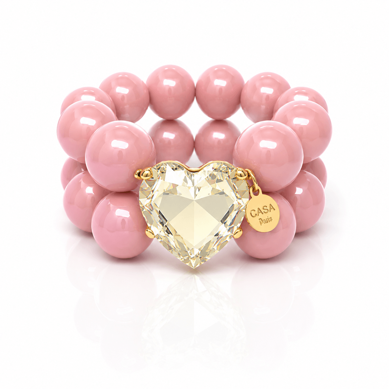 Armband aus glänzenden rosa Resin-Perlen mit großem facettiertem Kristallherz goldfarbener Fassung und rundem Casapari-Anhänger auf weißem Hintergrund.