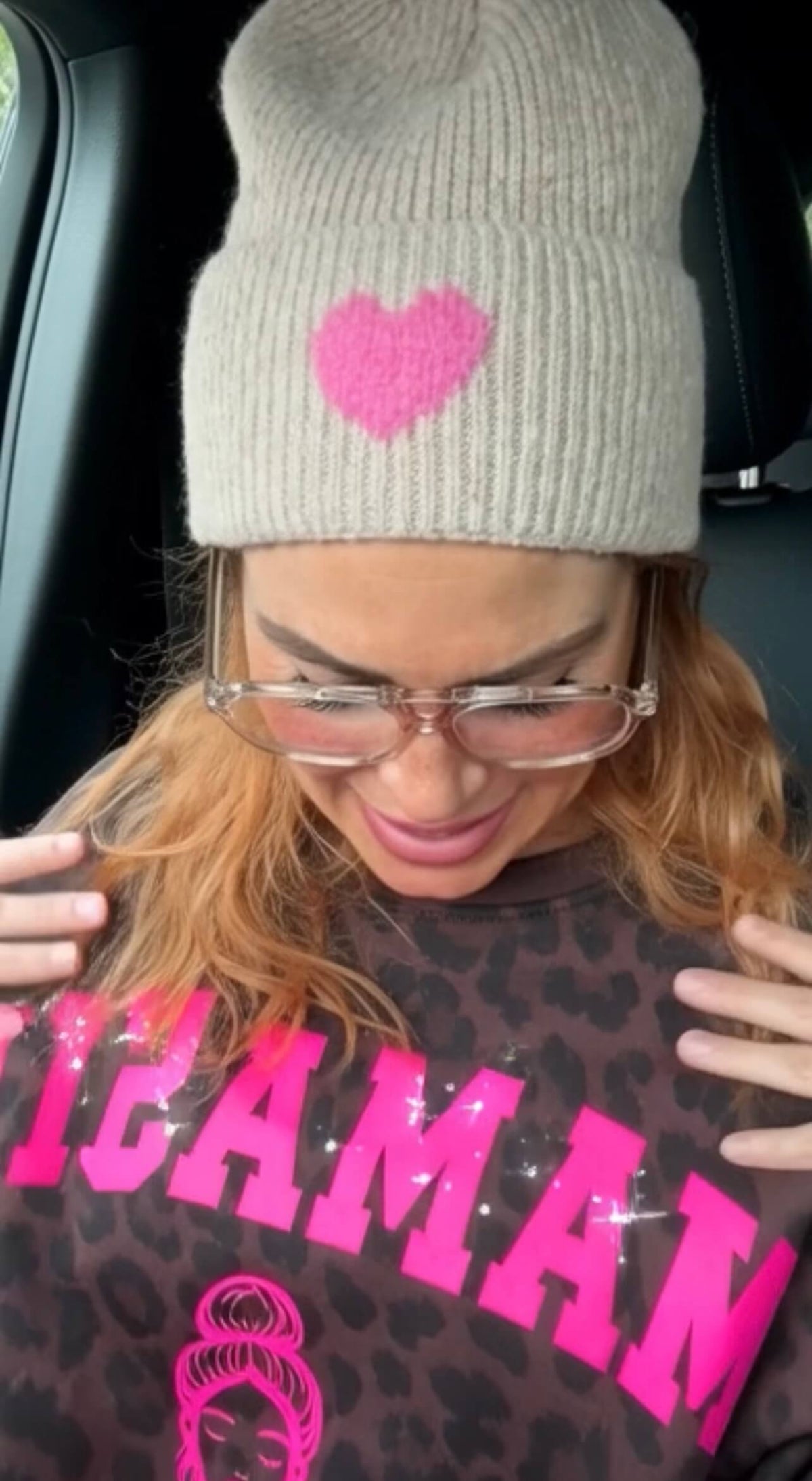 Frau trägt eine beige Strick-Beanie mit pinkfarbenem Herz, transparente Brille und ein Leo-Sweatshirt mit auffälligem pinkfarbenem Statement-Print.