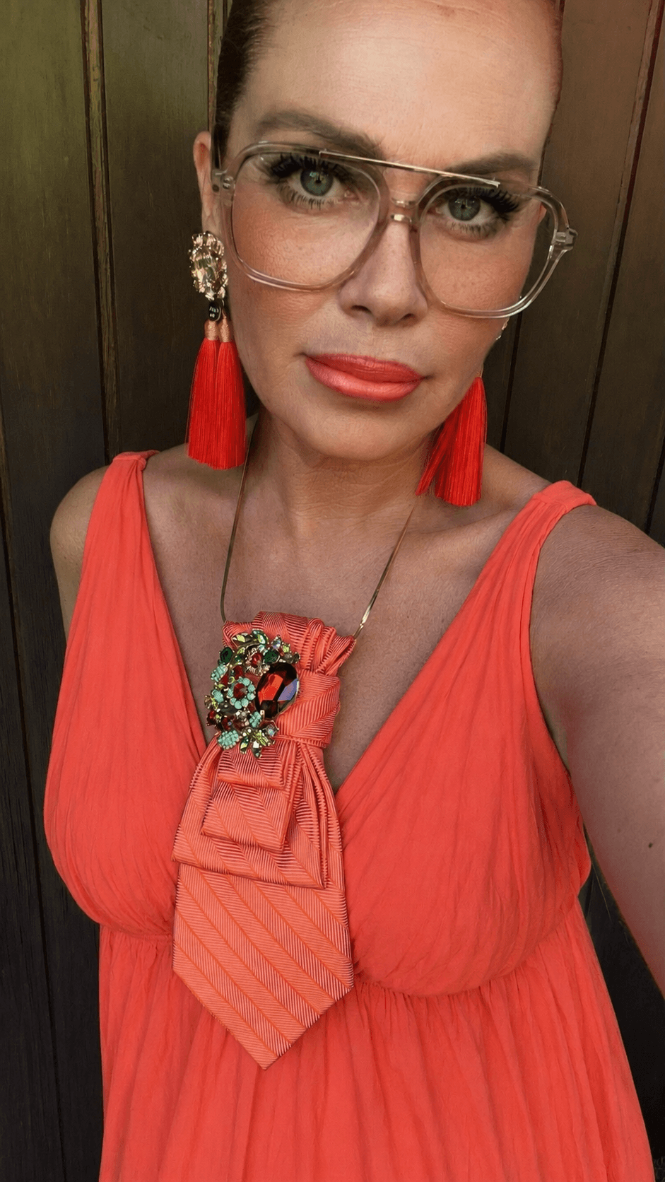 Frau mit korallfarbenem Sommerkleid, roten Quastenohrringen und korallfarbener Casapari-Krawatte mit Schmuckbrosche.