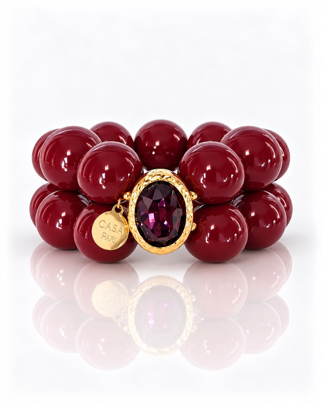 Crystal Berry Armband mit zwei Reihen beerenroter Perlen, facettiertem violettem Kristall in goldfarbener Fassung und Casa Pari Anhänger, gerade und mittig auf weißem Hintergrund.