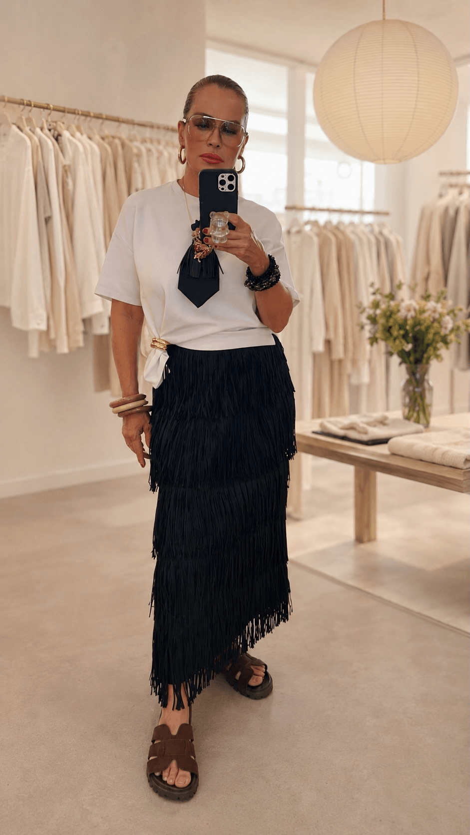 Frau trägt einen schwarzen Fransenrock mit weißem T-Shirt und Statement-Krawatte in einer hellen Boutique.