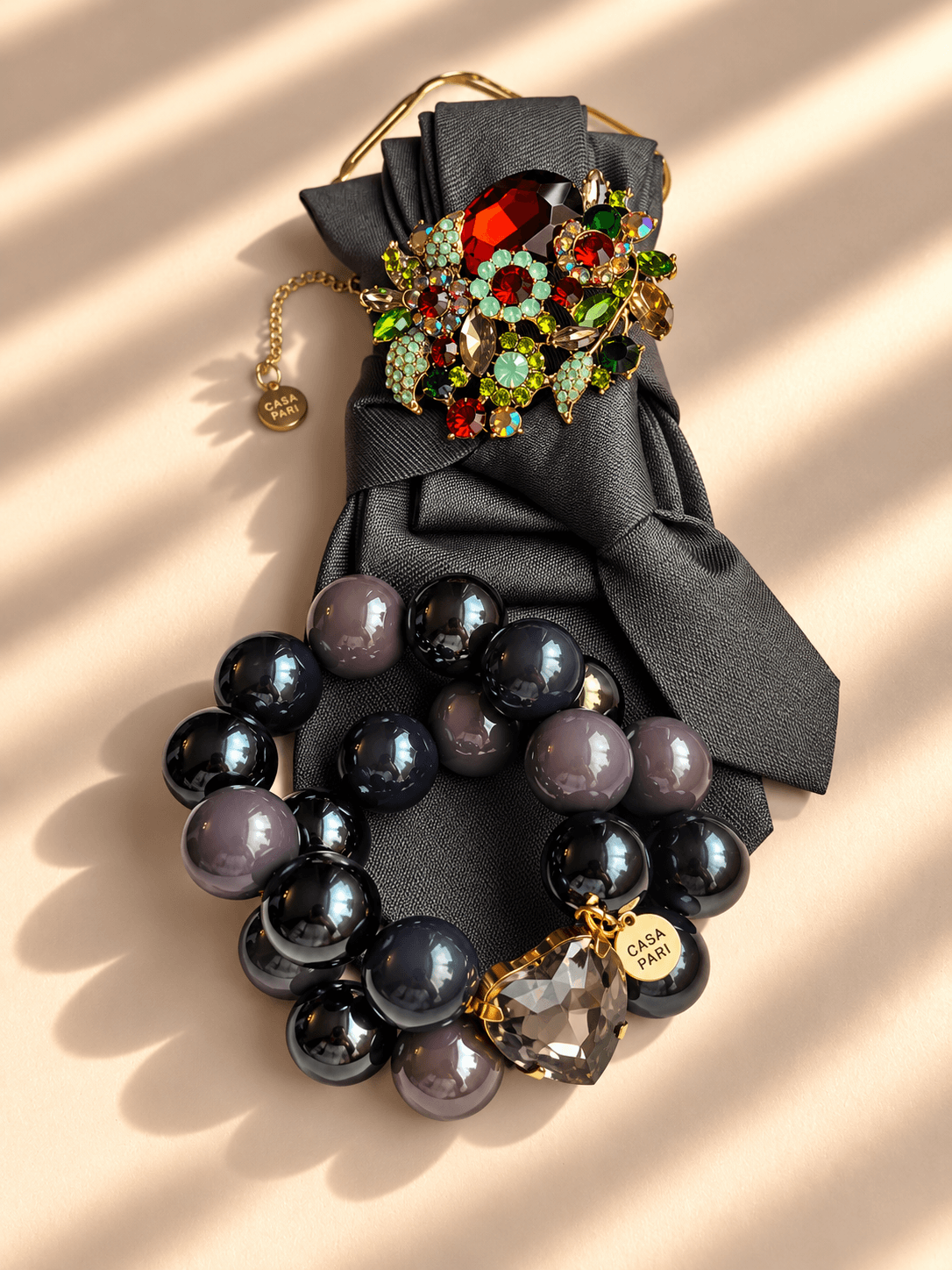 Silk Affair Armband Smoky Grey von Casapari mit großen Perlen in Rauchgrau und Schwarz, Crystal Heart und goldenen Details, kombiniert mit grauer Statement-Krawatte.