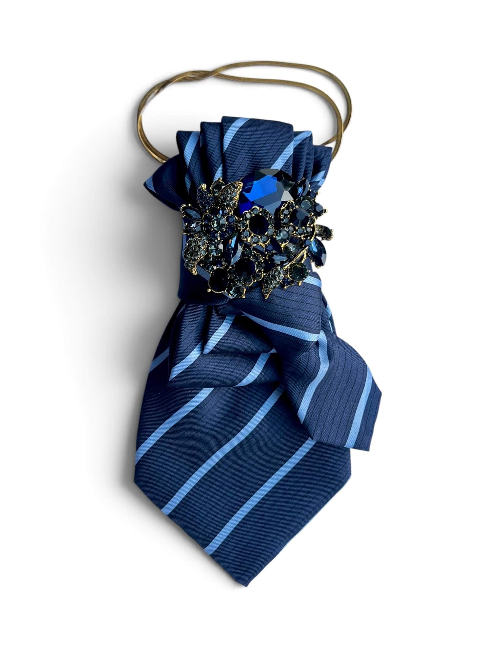 Dunkelblaue Statement-Krawatte mit goldfarbener Schmuckbrosche in Türkis- und Blautönen sowie feiner Halskette.