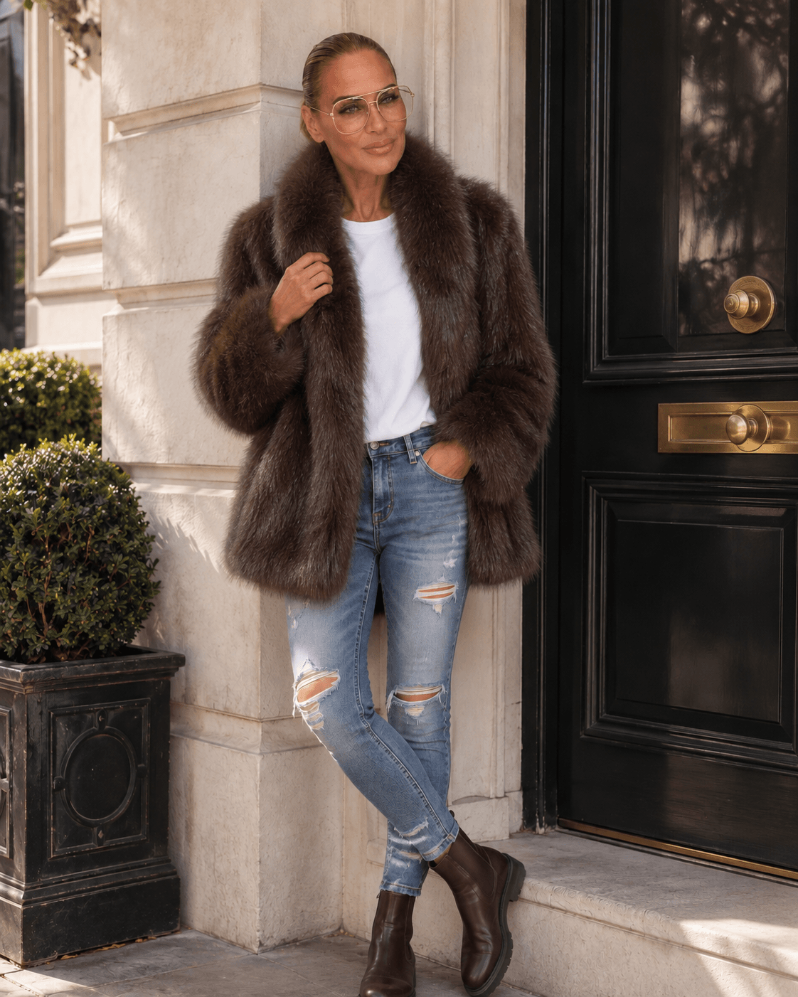 Frau trägt dunkelbraune Fake-Fur-Jacke mit großem Reverskragen, weißem T-Shirt, Used Jeans und braunen Chelsea Boots.