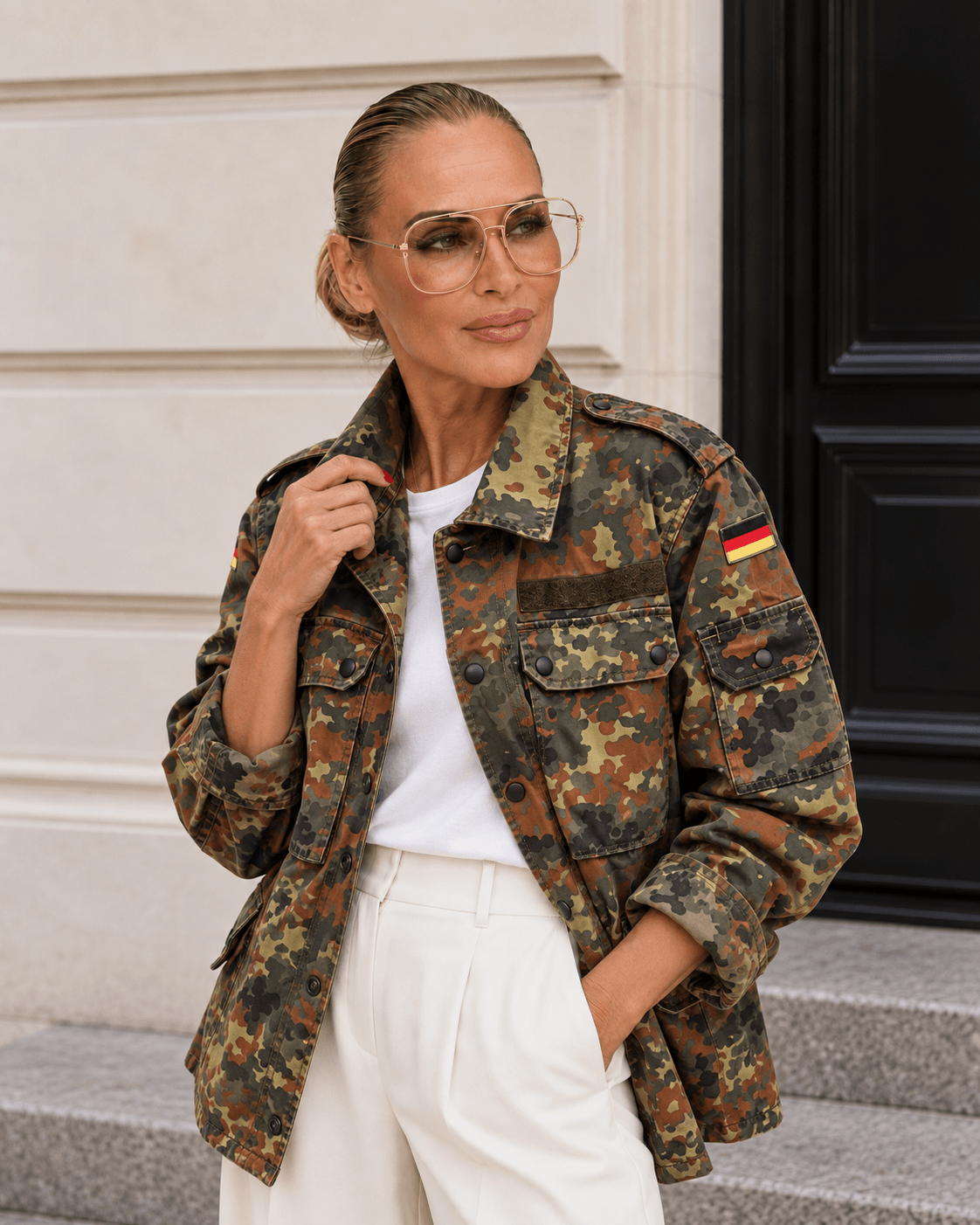 Model trägt die Vintage Military Jacket Army Love im Flecktarn mit weißem Shirt und weißer Marlene; eine Hand hält lässig den Kragen.