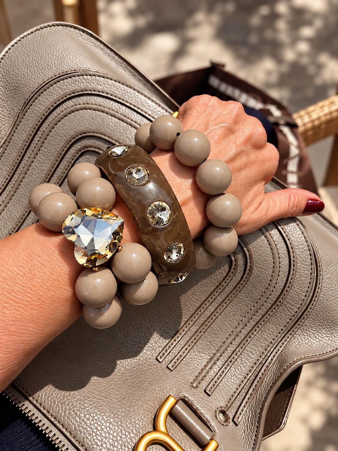 Drei Armbänder in Cashmere Grey am Handgelenk: Crystal Heart Armband, schlichtes Perlenarmband und Resin-Bangle mit Kristallsteinen.