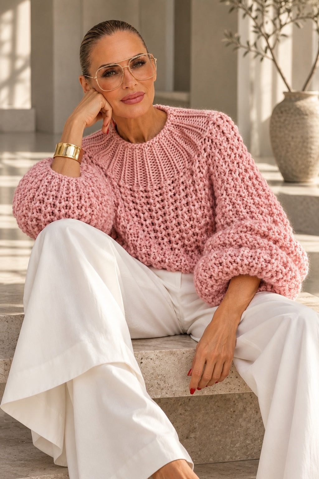 Model im rosa Chunky-Knit-Pullover mit weißer Marlenehose auf Steinstufen