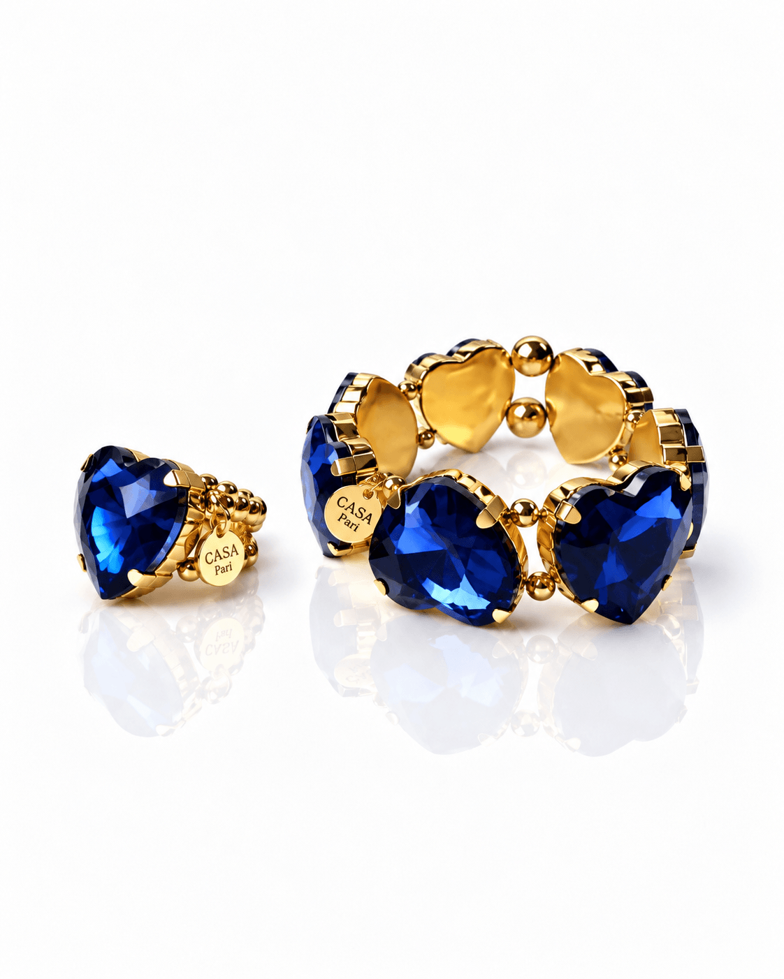 Herzring mit goldenen Perlen und dazu passend ein Armband aus komplett Herzen in blau in Goldfassung auf weißem Hintergrund fotografiert