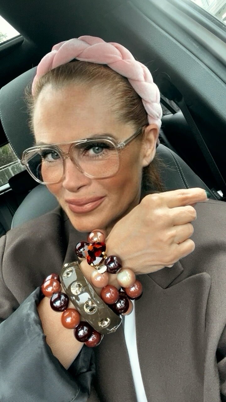 Frau mit pinkem Haarreif trägt mehrere Crystal Hearts Armbänder in warmen Braun-, Rosé- und Burgundertönen sowie einen Strass-Armreif.