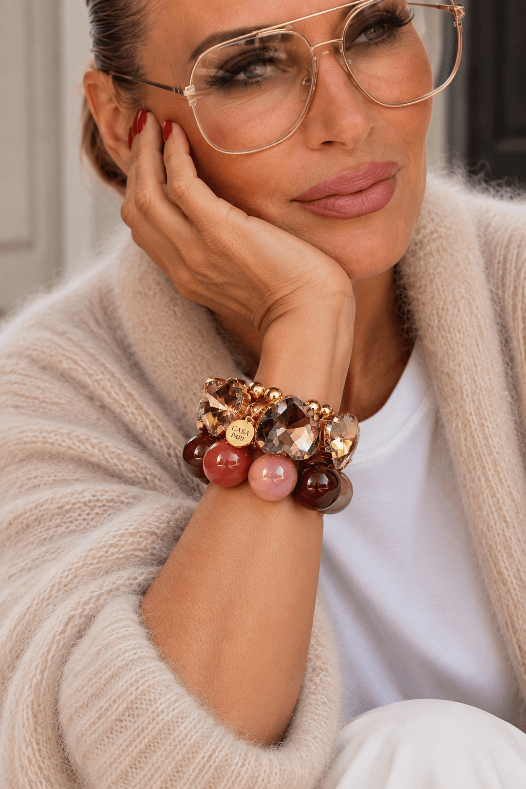 Frau trägt zwei Armbänder in bunten Farben, hat ne beige Kid Mohair an und hält ihre Hand ans Gesicht