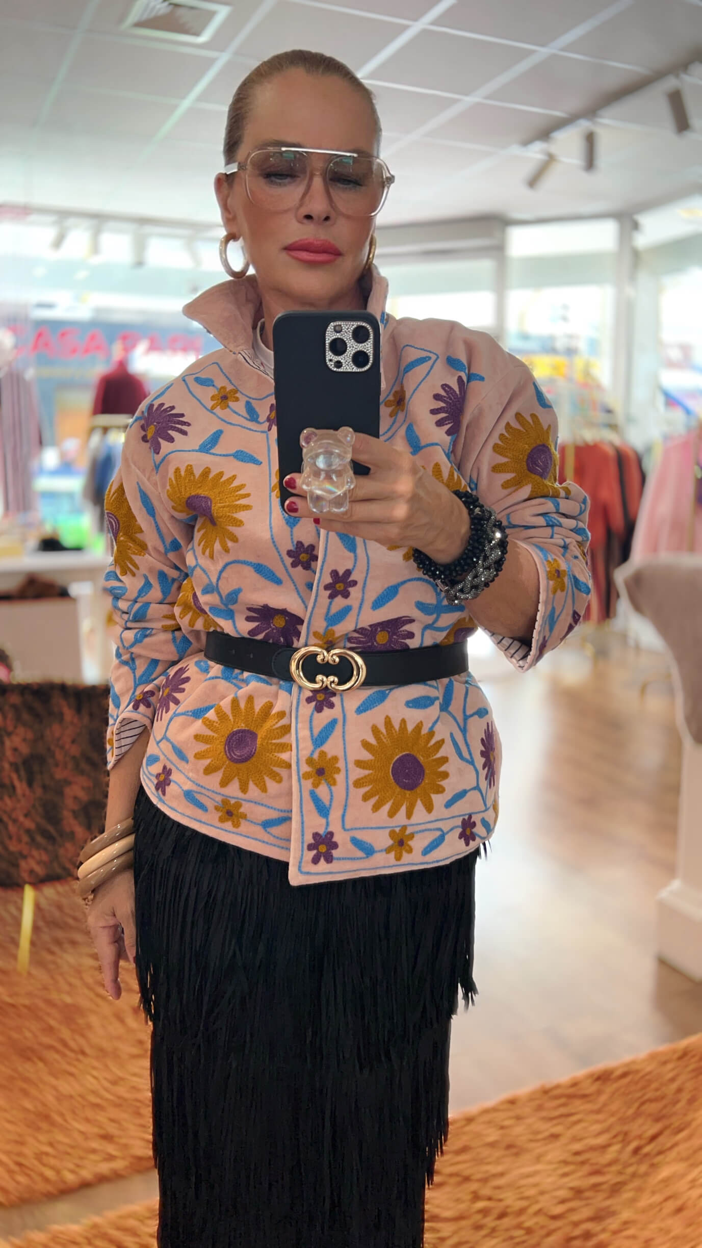 Frau trägt die Embroidered Couture Jacke Powder Bloom mit floraler Stickerei, kombiniert mit schwarzem Gürtel und schwarzem Fransenrock.