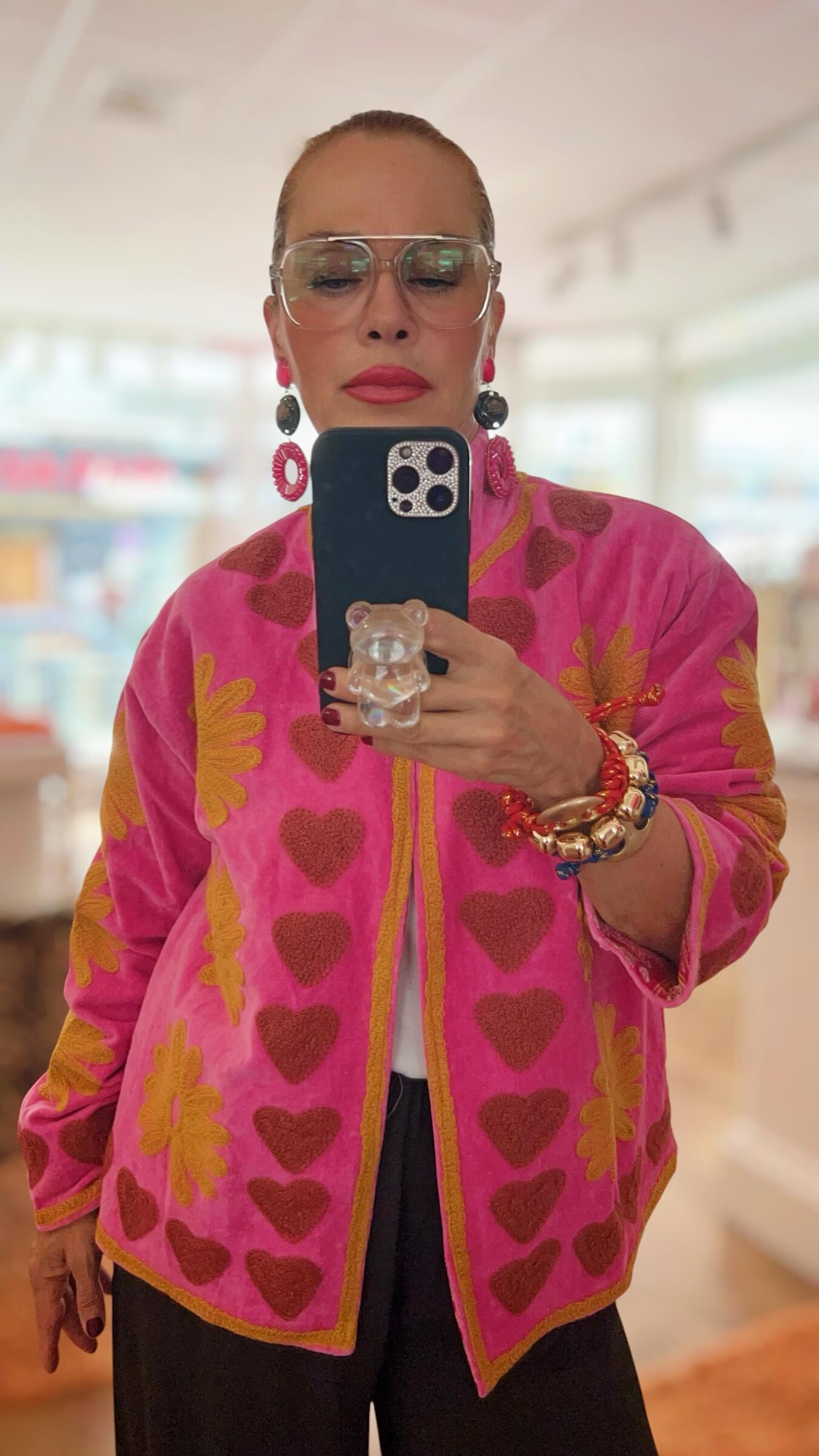 Pinkfarbene Embroidery-Jacke mit karamellfarbenen Herz- und Blumenstickereien, offen getragen über einem weißen Oberteil.