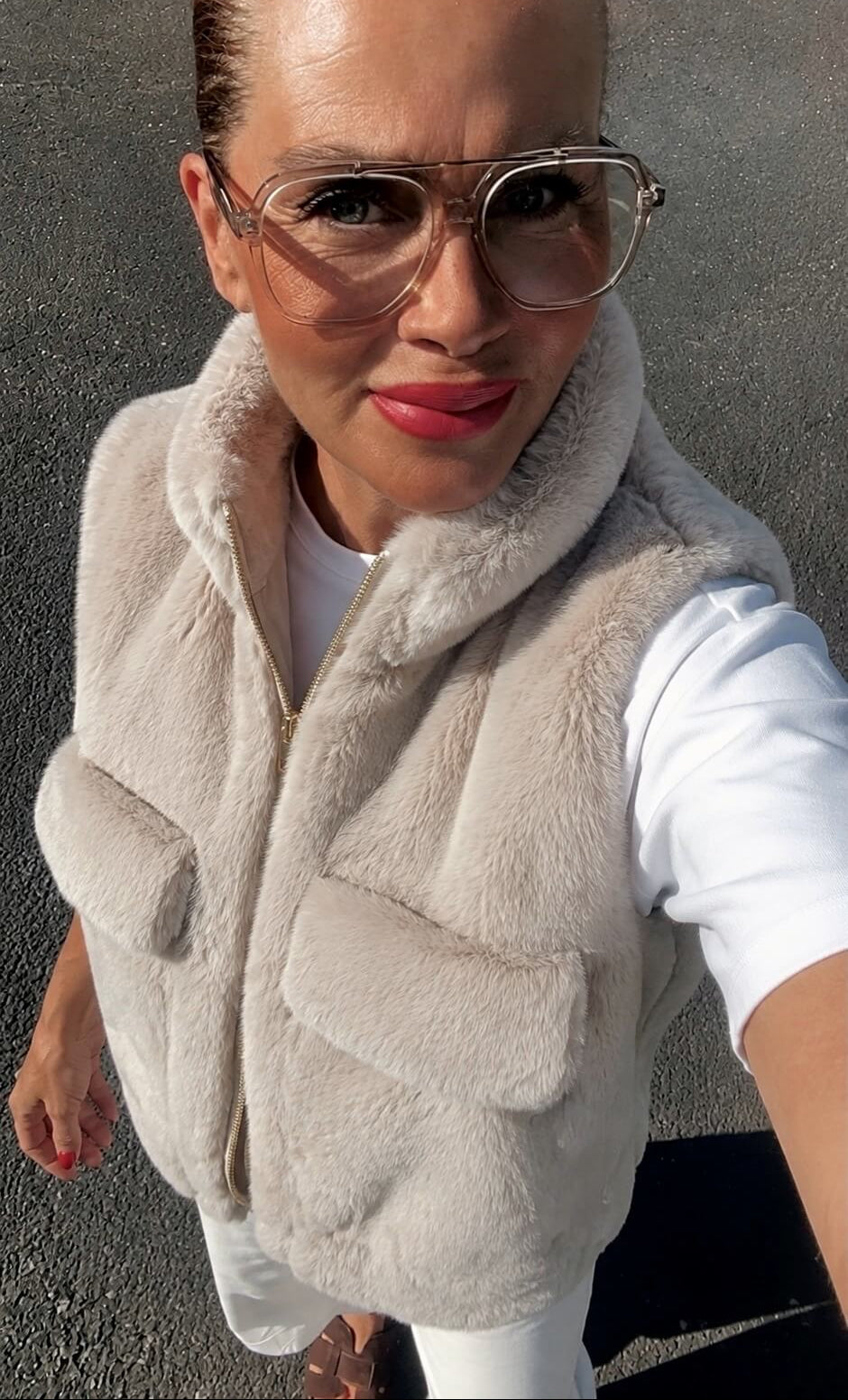 Frau trägt eine beige CASAPARI Fake-Fur-Weste mit goldfarbenem Reißverschluss über einem weißen T-Shirt.