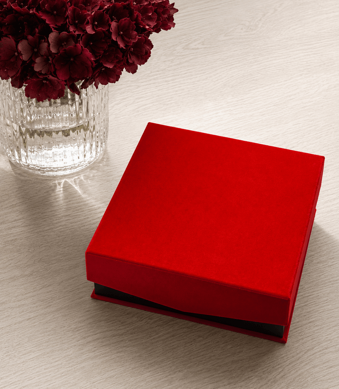 Geschlossene rote Geschenkebox von CASAPARI auf einem hellen Holztisch neben einer Vase mit burgunderfarbenen Hortensien.
