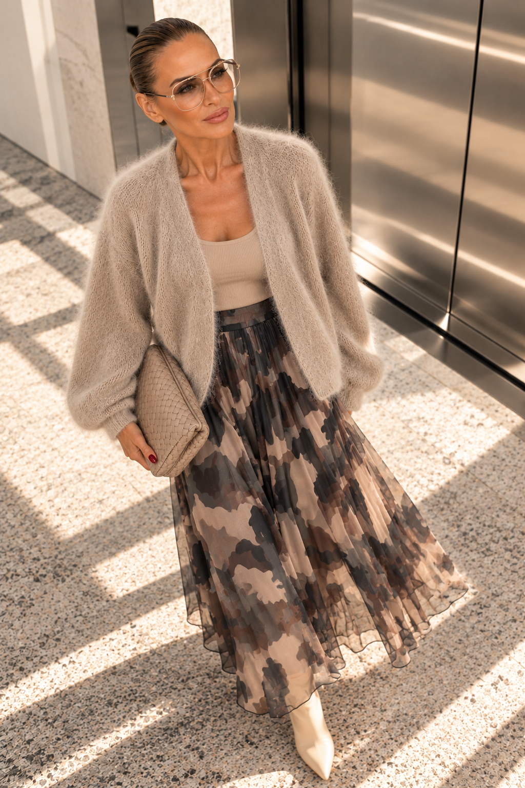 KI-Model mit offener Kid-Mohair-Strickjacke in Taupe und Camouflage-Rock vor einem Aufzug