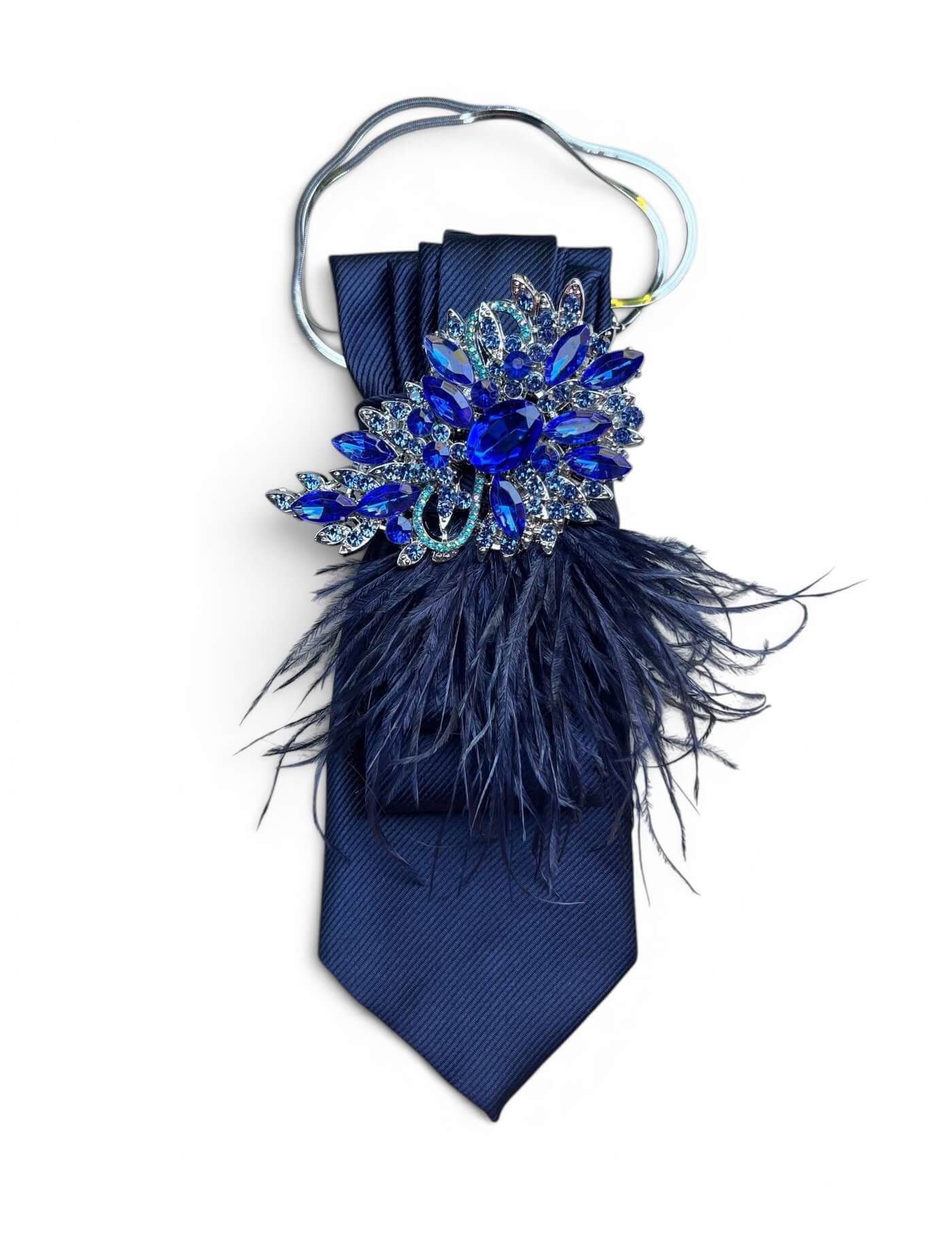 Dunkelblaue Krawatte mit opulenter blauer Kristallbrosche, dunklen Federn und silberfarbenem Tragebügel auf hellem Hintergrund.