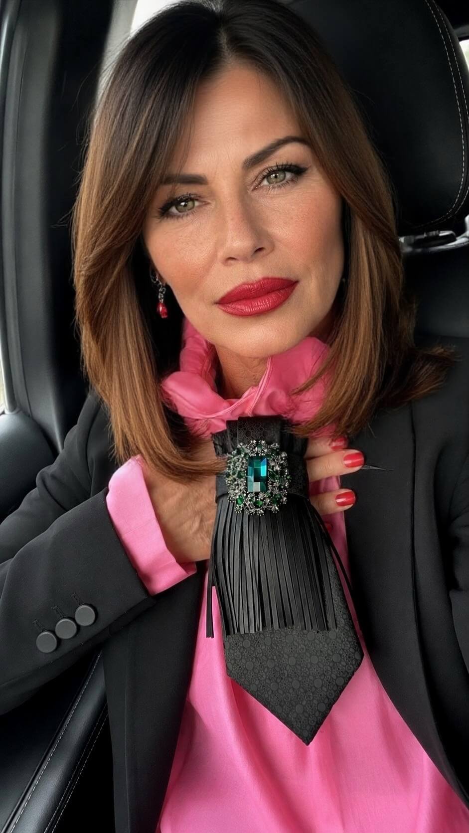 Schwarze Krawatte aus Vintage-Seide mit feinem Muster, schwarzem Fransenbesatz, silberfarbener Kette und smaragdgrüner Schmuckbrosche, getragen zu einer pinken Bluse und einem schwarzen Blazer.