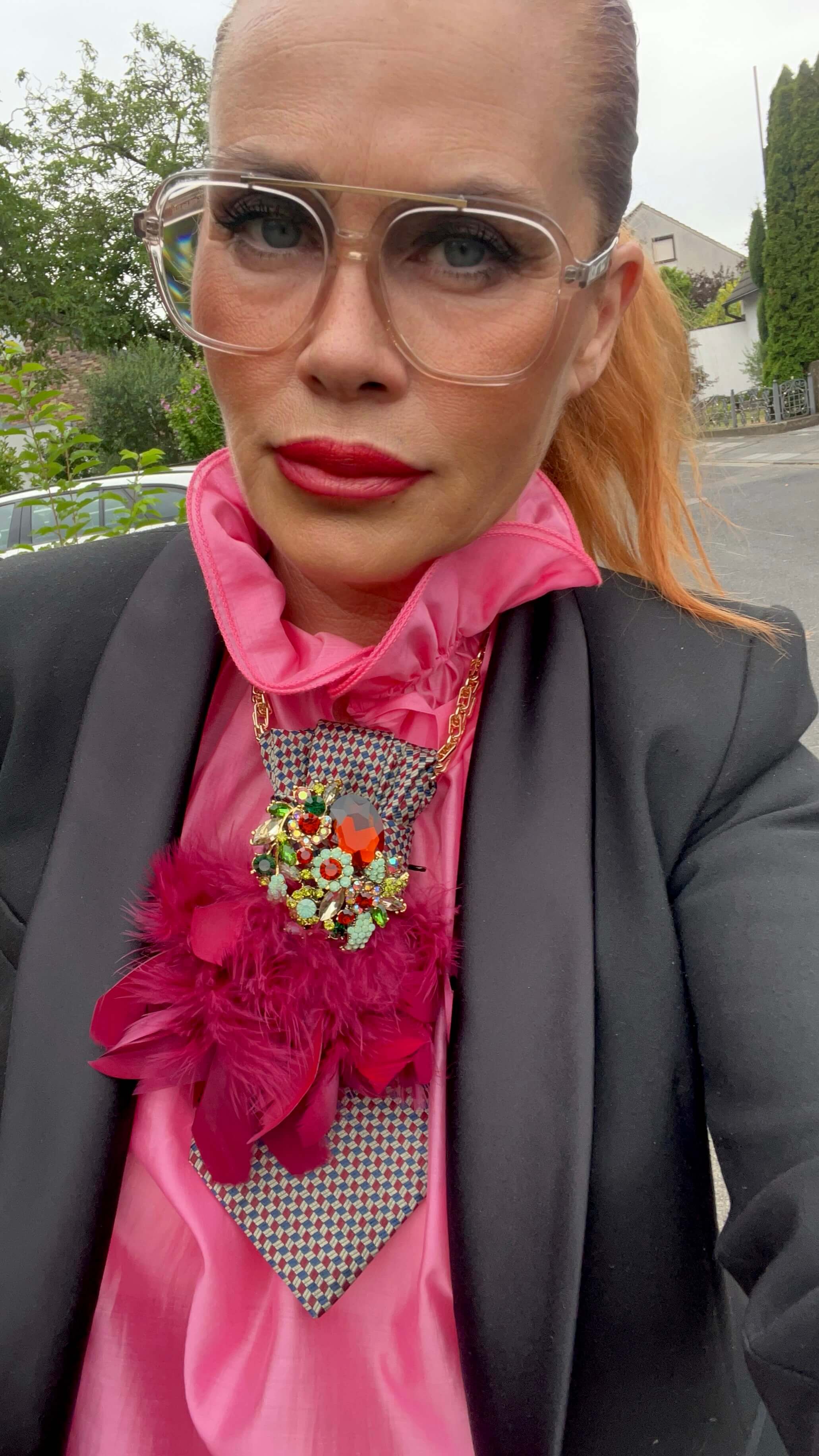 Vintage-Seidenkrawatte mit feinem Muster, bordeauxfarbener Federbrosche und großer Schmuckbrosche, getragen zu einer pinken Bluse und einem schwarzen Blazer.