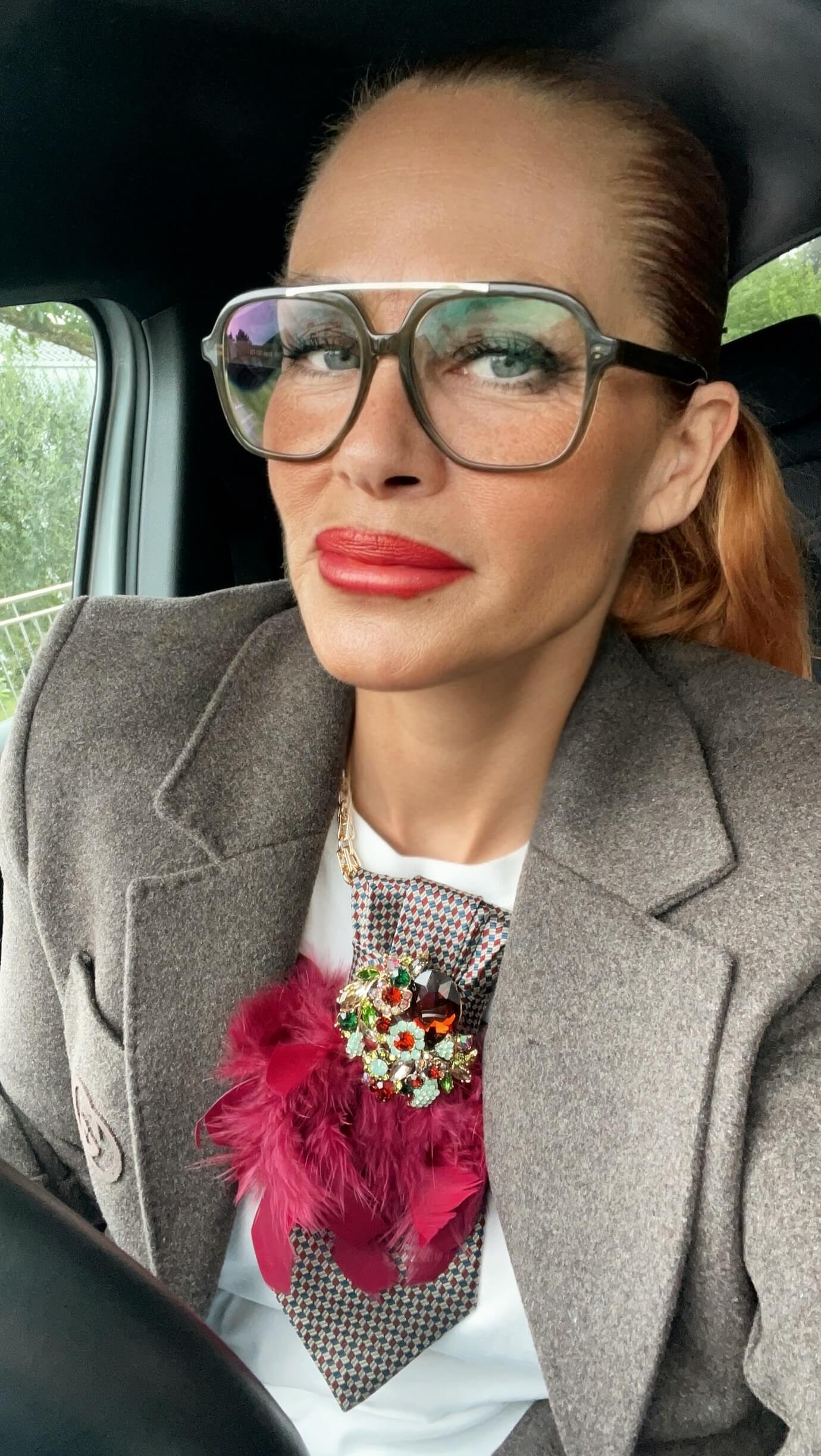 Vintage-Seidenkrawatte mit geometrischem Muster, bordeauxfarbener Federbrosche und funkelnder Schmuckbrosche, kombiniert mit weißem Oberteil und grauem Blazer.