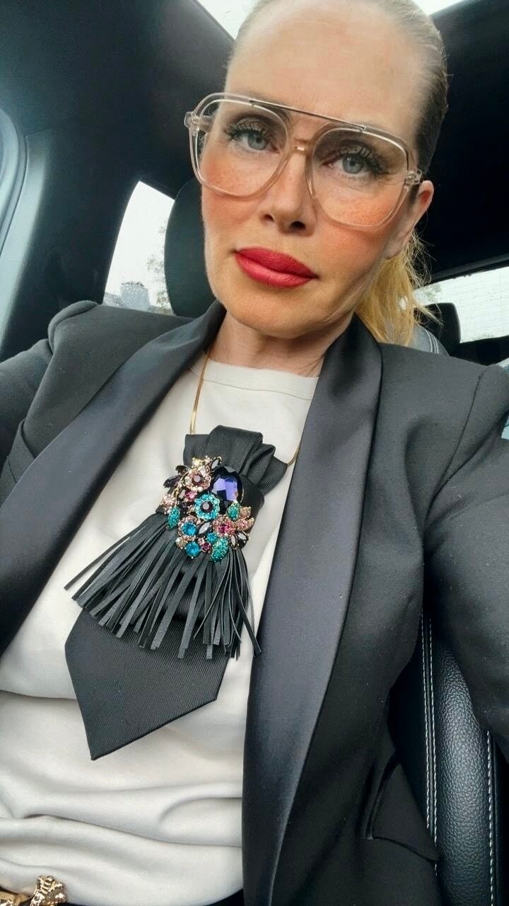 Detailansicht einer schwarzen Vintage-Krawatte mit dekorativer Brosche und Fransen-Detail, getragen mit schwarzem Blazer.