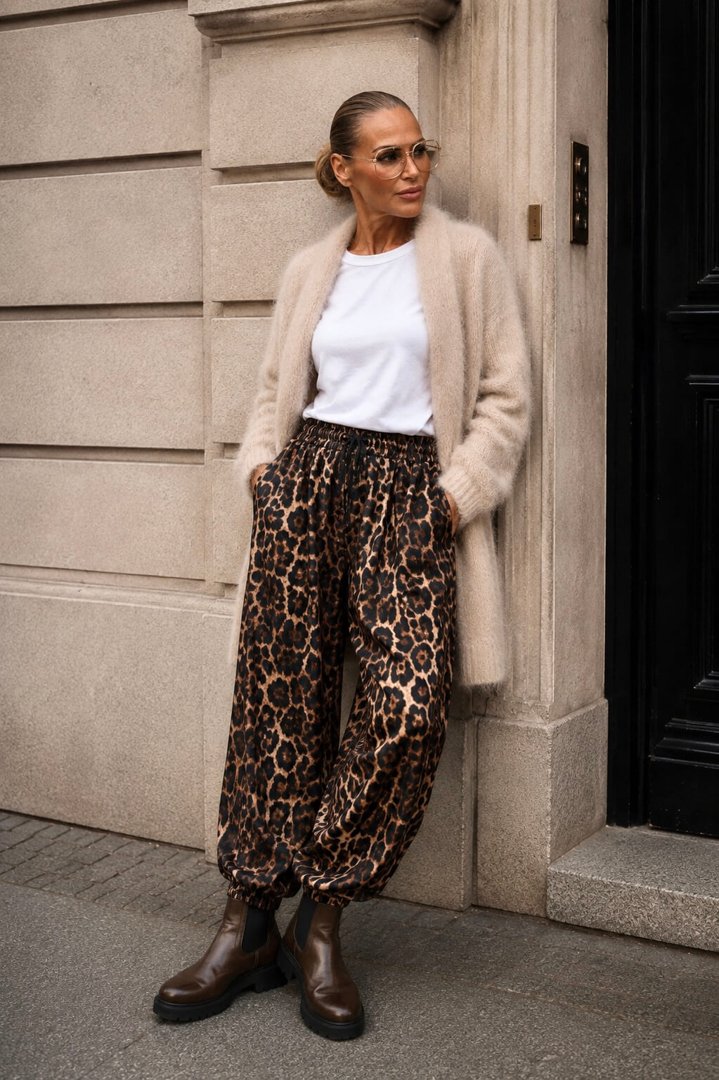 Frau trägt lässige Leo-Hose mit Gummizug am Bein, weißem Shirt, beigem Cardigan und braunen Chelsea Boots.