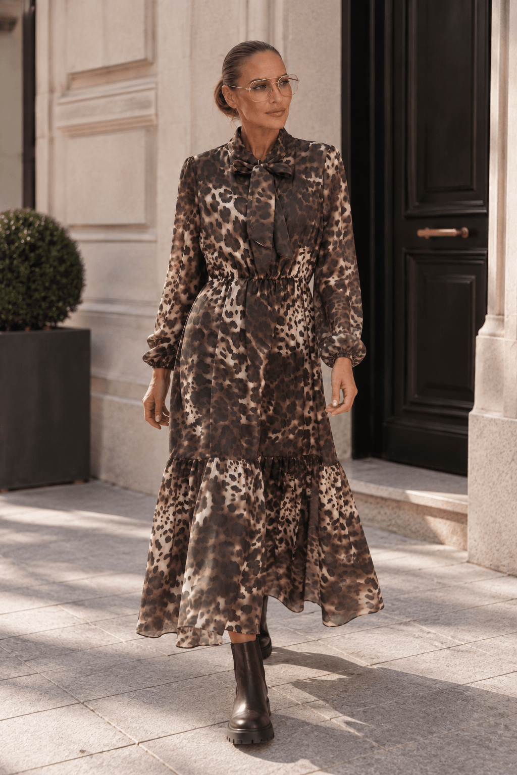 Frau trägt langes braunes Leo-Kleid mit Schluppe und dunklen Chelsea Boots.