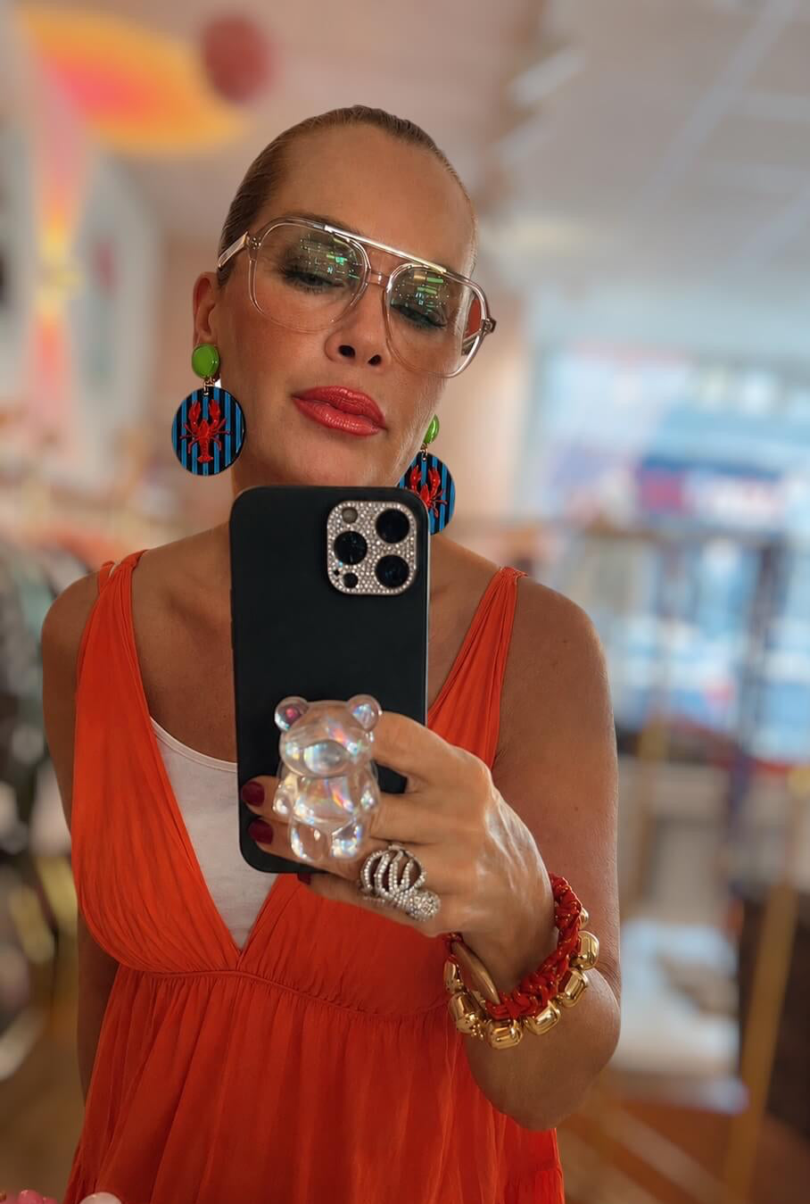 Frau trägt ein orangefarbenes Kleid, macht ein Selfie und fotografiert die lOhrringe aufgenommen in einer Boutique