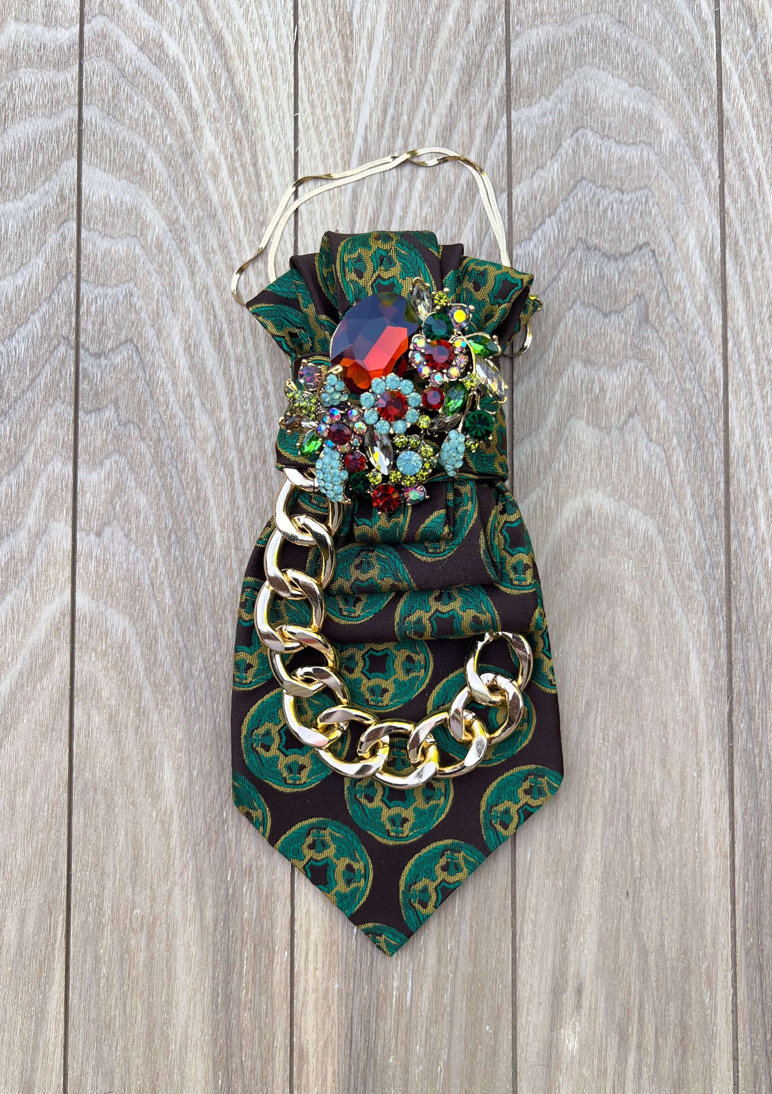 Vintage-Krawatte in Dunkelbraun mit grün-goldenem Ornamentmuster, großer Schmuckbrosche mit bunten Kristallen und goldfarbener Kette