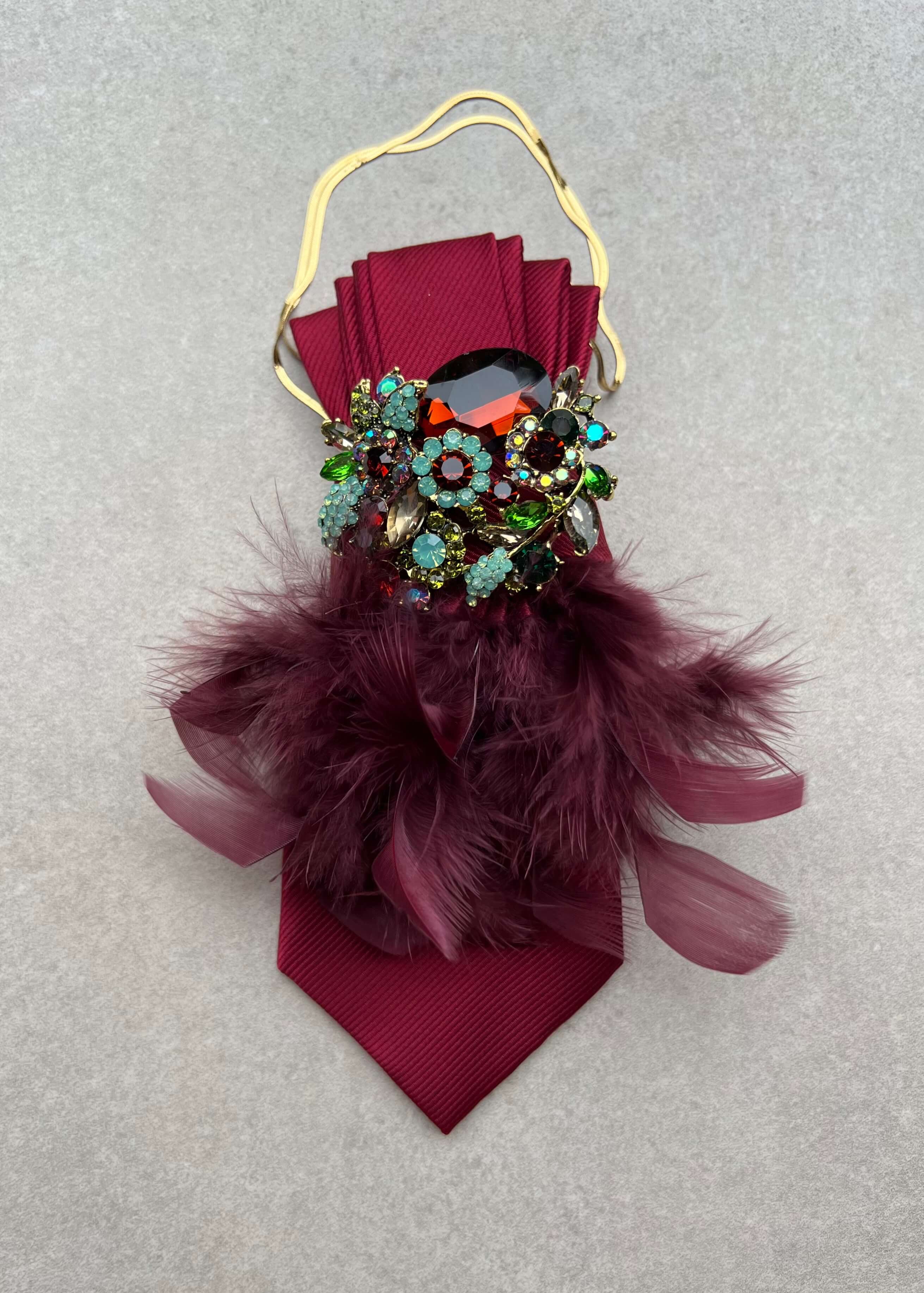 Bordeauxrote Feather-Affair-Krawatte mit goldfarbener Kette, opulenter Kristallbrosche in Rot, Türkis und Grün sowie bordeauxfarbenen Federn