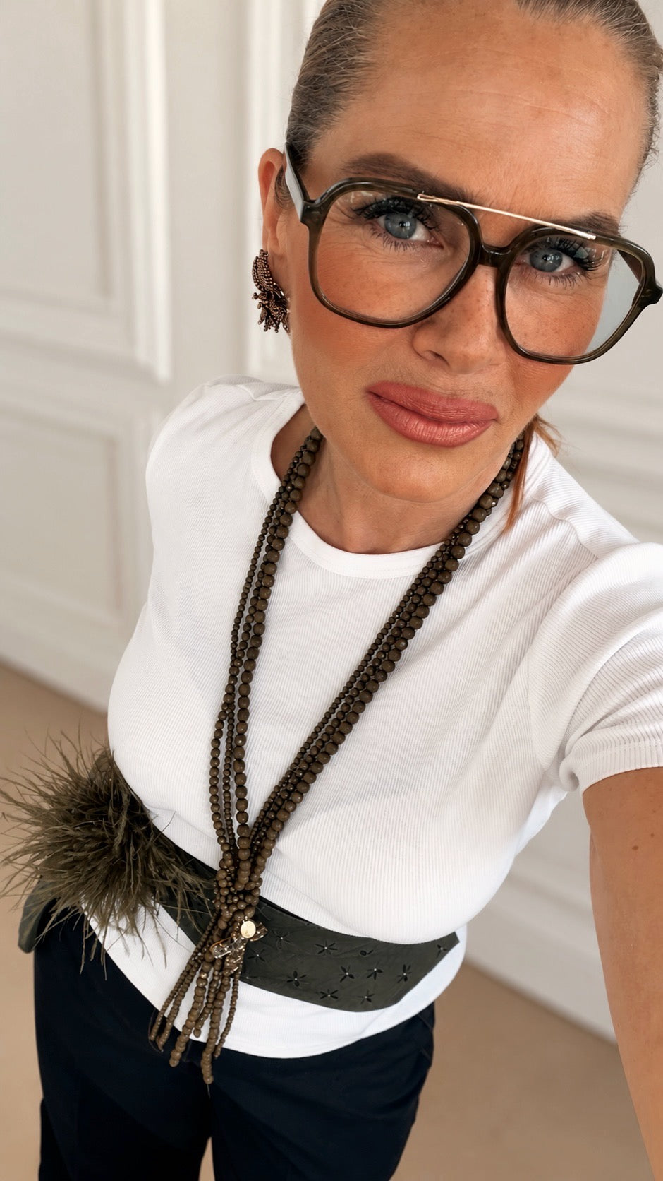 Olivfarbene Cross Necklace Gil am Model mit weißem Shirt und bronzefarbenen Ohrringen