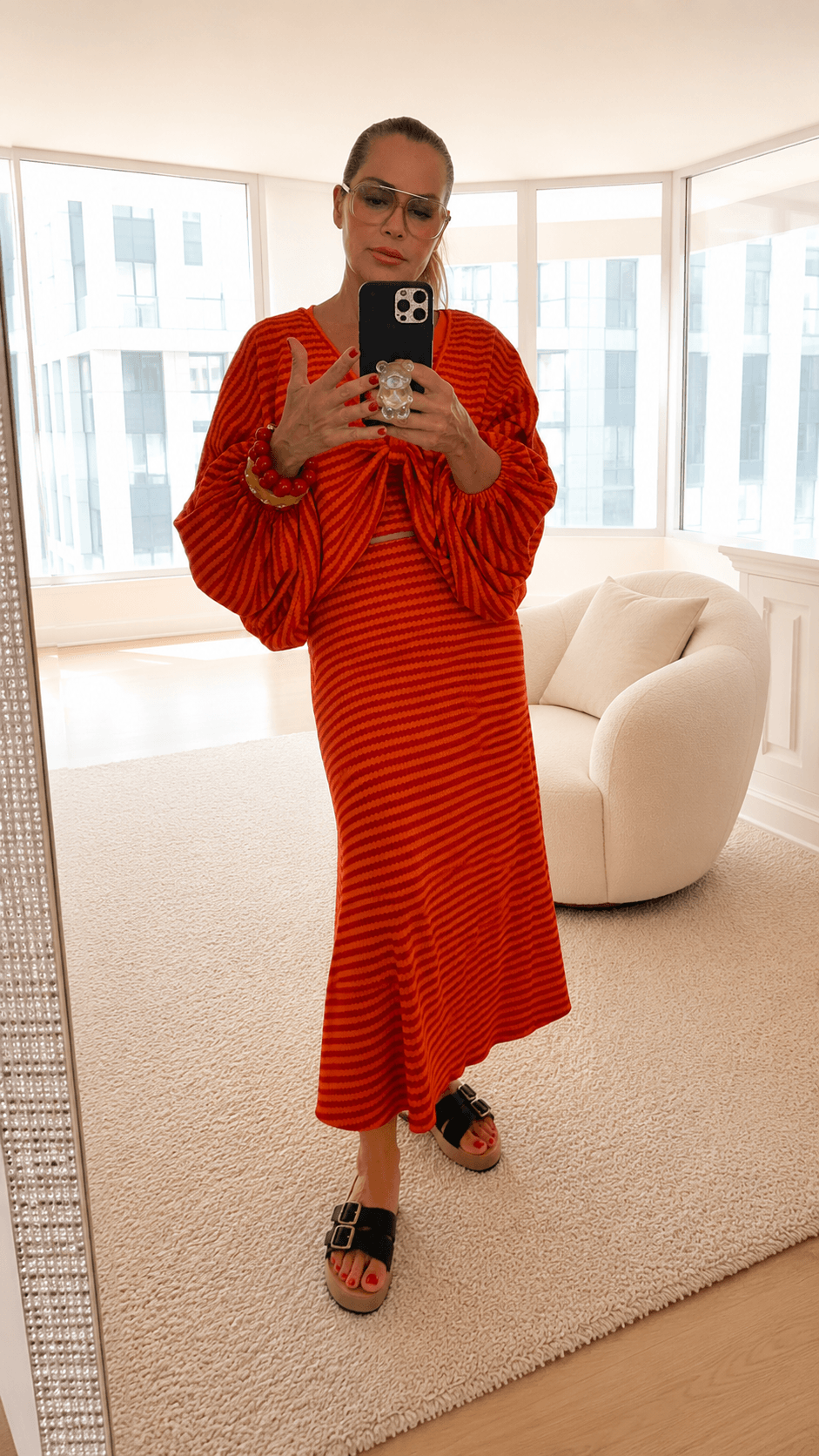 Model trägt ein dreiteiliges Set in Orange und Rot mit gestreiftem Muster. Das Set besteht aus einem Tanktop, einem locker fallenden Fledermaus-Pullover mit Raffung vorne sowie einem langen Rock in A-Linie.