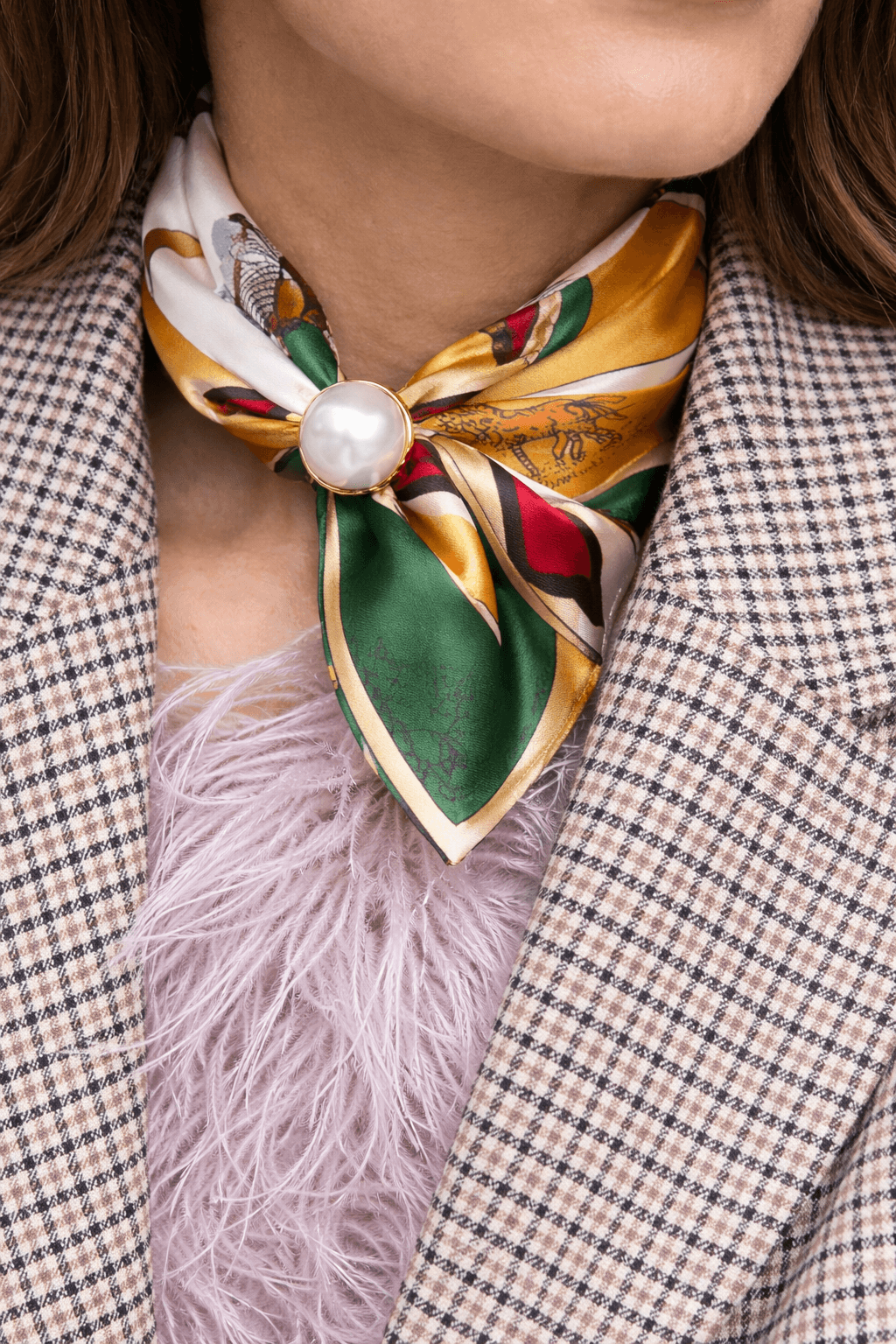 Seidentuch mit mehrfarbigem Muster in Grün, Gold, Rot und Beige, als Halstuch gebunden und mit einer großen weißen Perle als Verschluss getragen, kombiniert mit kariertem Blazer und hellem Oberteil.