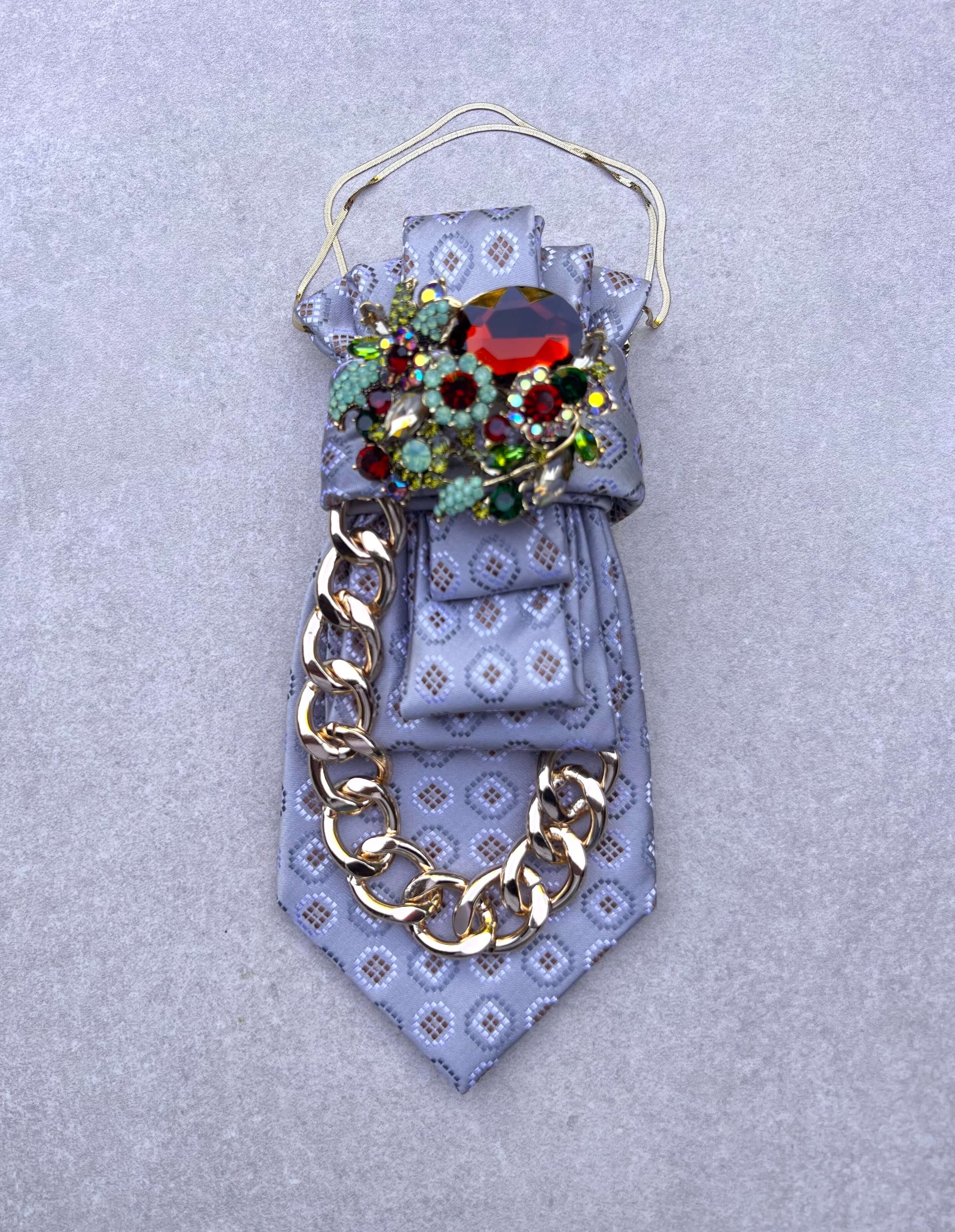 Silbergraue Krawatte mit dezentem Muster, goldfarbener Gliederkette und funkelnder Kristallbrosche in Rot, Grün und Türkis