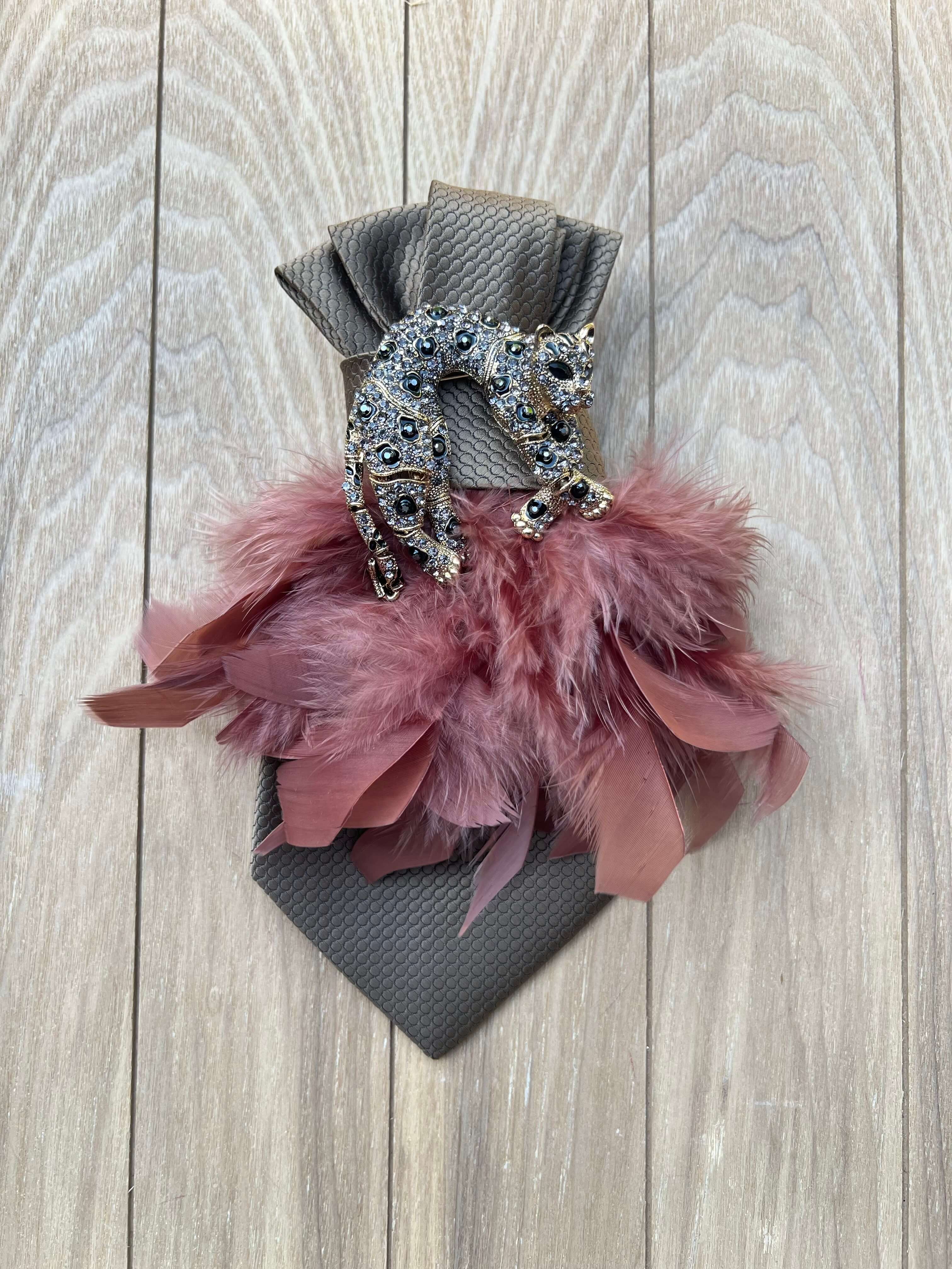 Graue Vintage-Seidenkrawatte mit Leopardenbrosche und roséfarbenen Federn auf hellem Holzhintergrund.