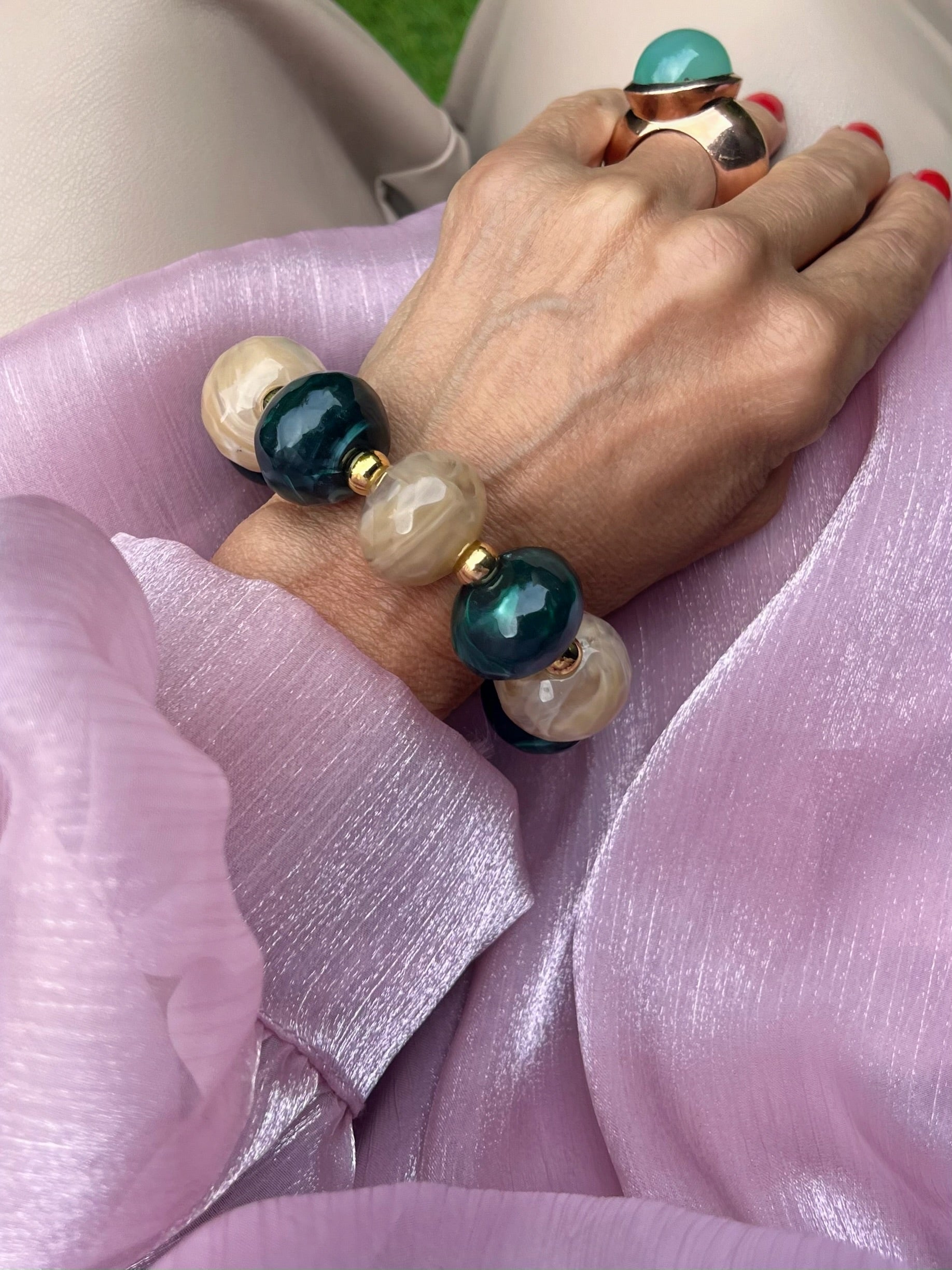 Großes Armband mit beigen und Olivenfarbenen Perlen an einem Handgelenk fotografiert auf Rosa Stoff.