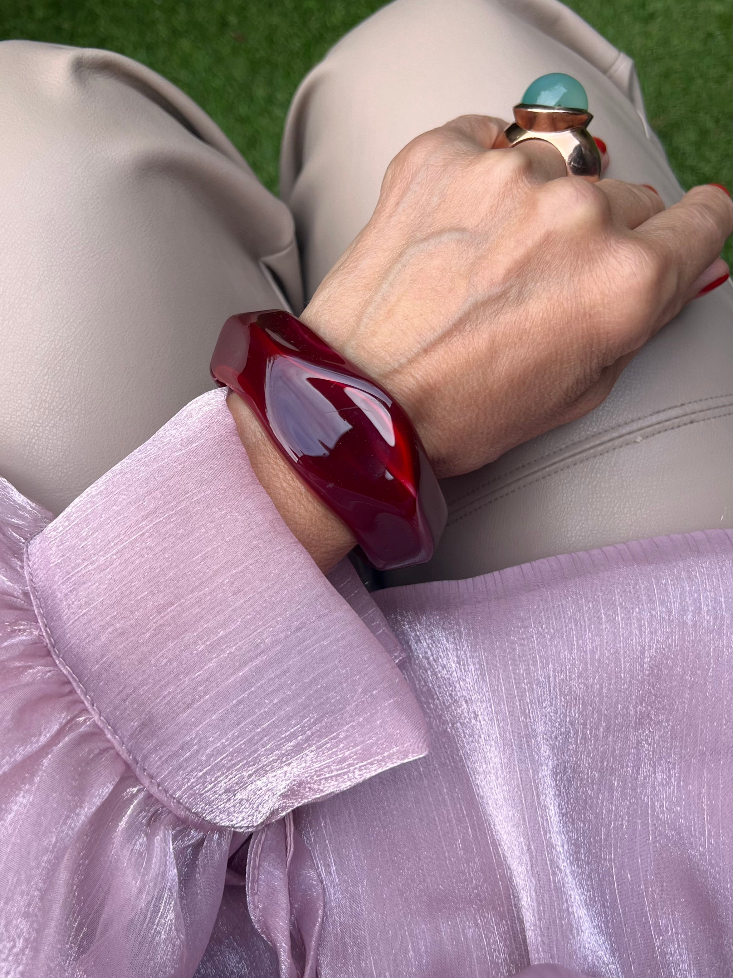 Armreifen in Burgunderfarben am Handgelenk mit großen Ring auf rosa Stoff fotografiert .