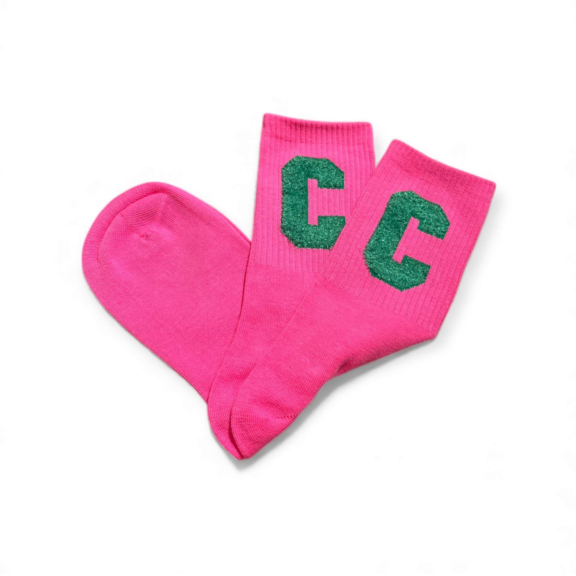 Pinke kurze Socken aus weichem Strick, flach liegend fotografiert, mit zwei grünem „C“-Buchstaben auf dem Schaft. Die Socken liegen leicht überkreuzt auf weißem Hintergrund.