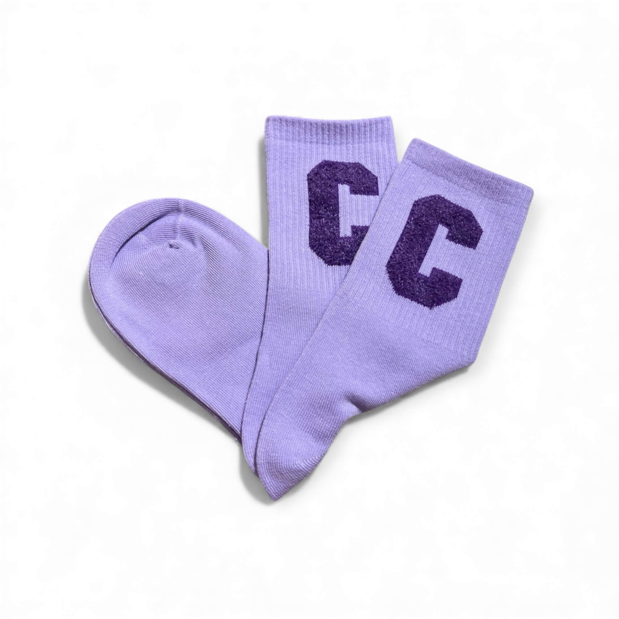 Fliederfarbene kurze Socken aus weichem Strick, flach liegend fotografiert, mit zwei lila „C“-Buchstaben auf dem Schaft. Die Socken liegen leicht überkreuzt auf weißem Hintergrund.