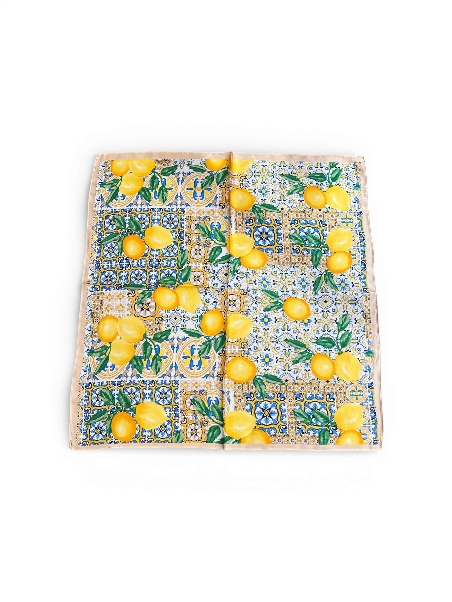 Quadratisches Tuch mit gelben Zitronen und blau-weißem Kachelmuster liegt flach ausgebreitet auf hellem Hintergrund.