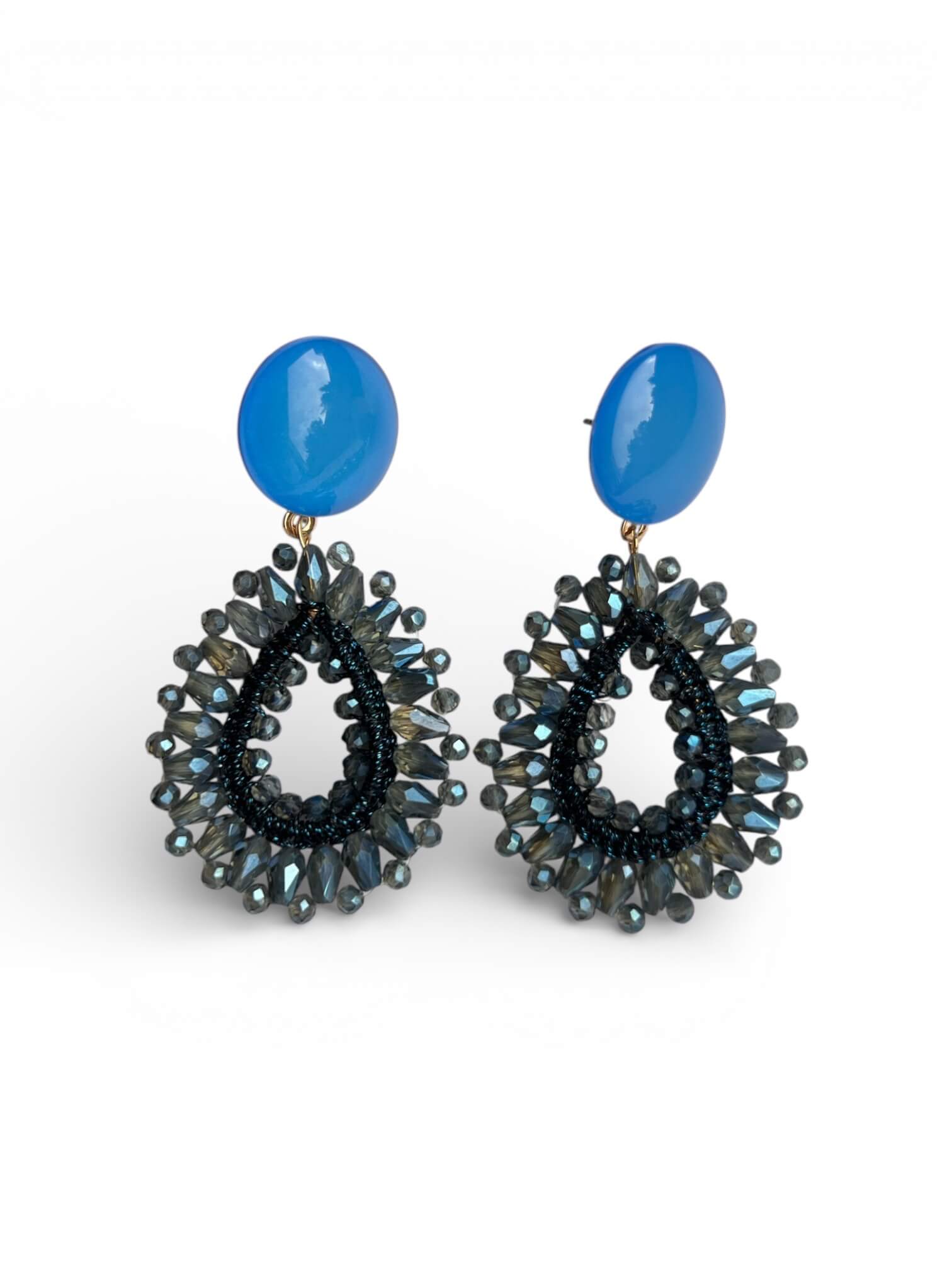 Paar blaue Garne-Ohrringe mit Glasperlen in Tropfenform vor hellem, neutralem Hintergrund.
