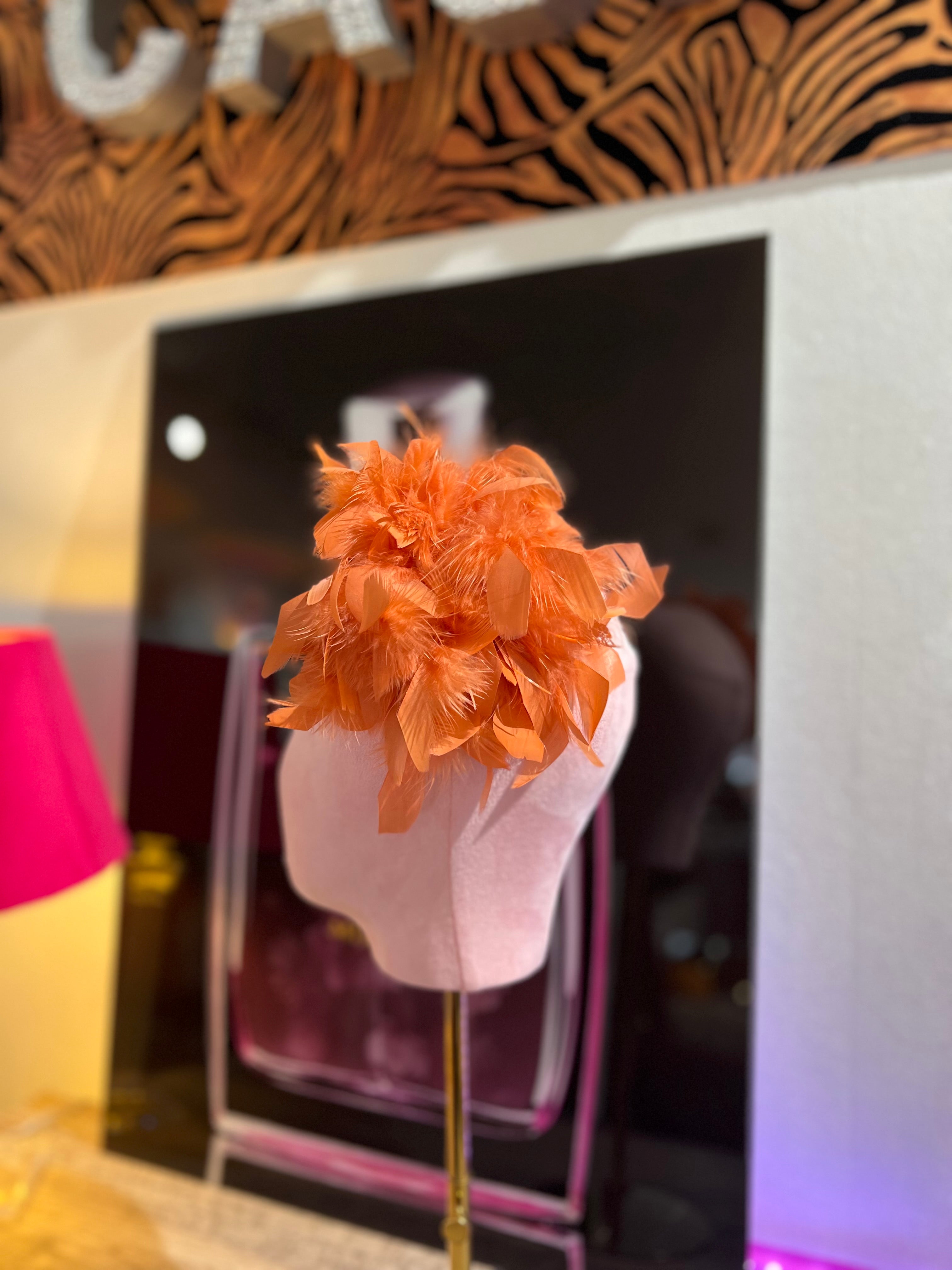Leuchtende orange Federbrosche, kunstvoll drapiert, präsentiert auf einem rosa Samt Kopf vor einer stilvollen Kulisse.