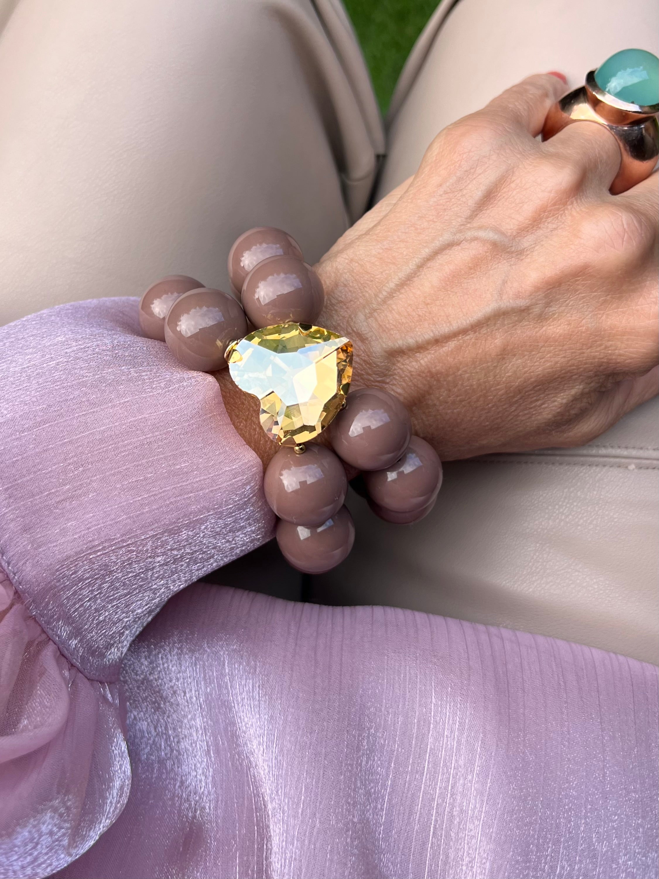 Armband in Taupe Farben mit großem Herzschmuckstein, und großer Ring. Am Handgelenk auf rosa Stoff fotografiert.
