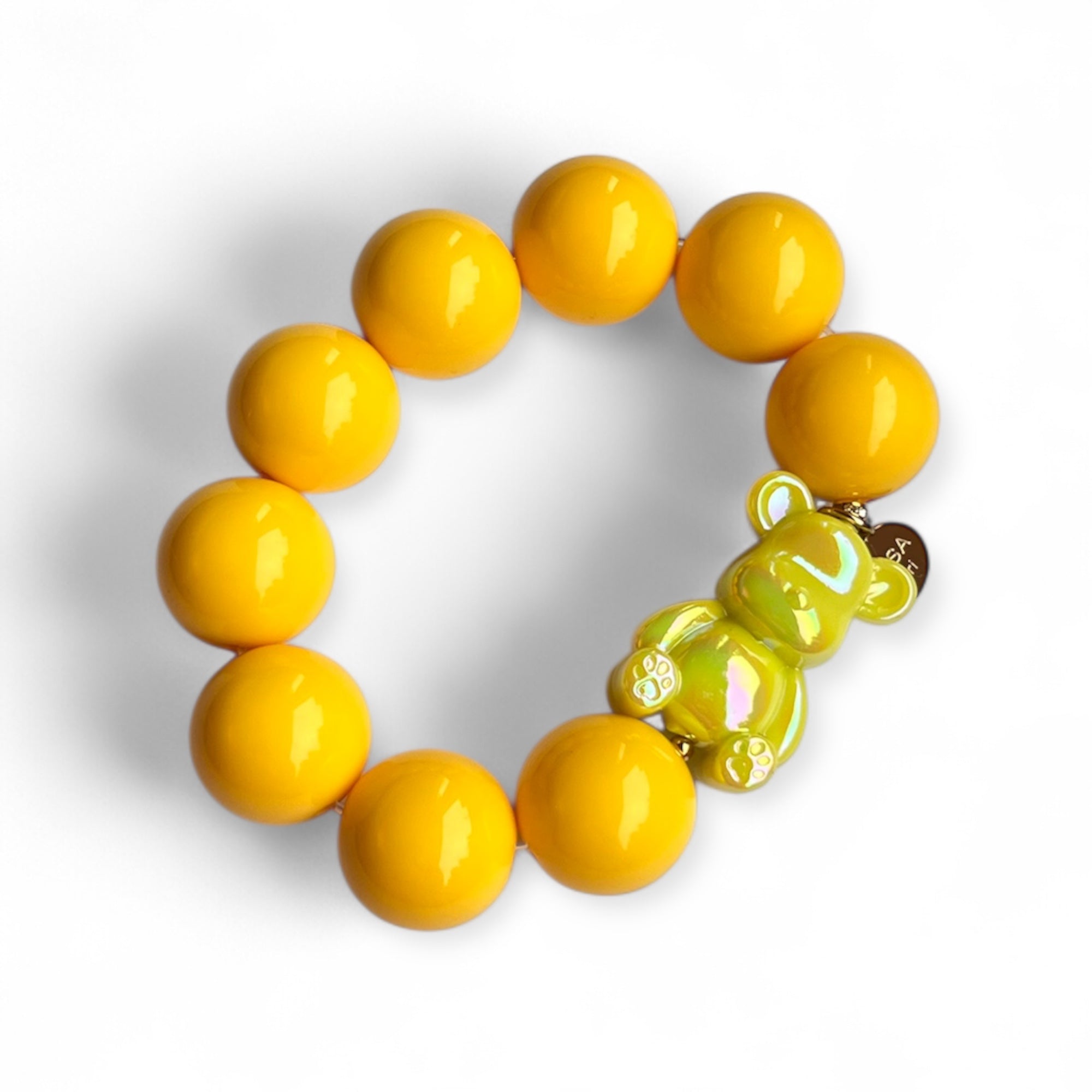 Armband aus gelben Kunstharzperlen mit einem kleinen schimmernden Bärenelement, handgefertigt von Casapari auf weißem Hintergrund.
