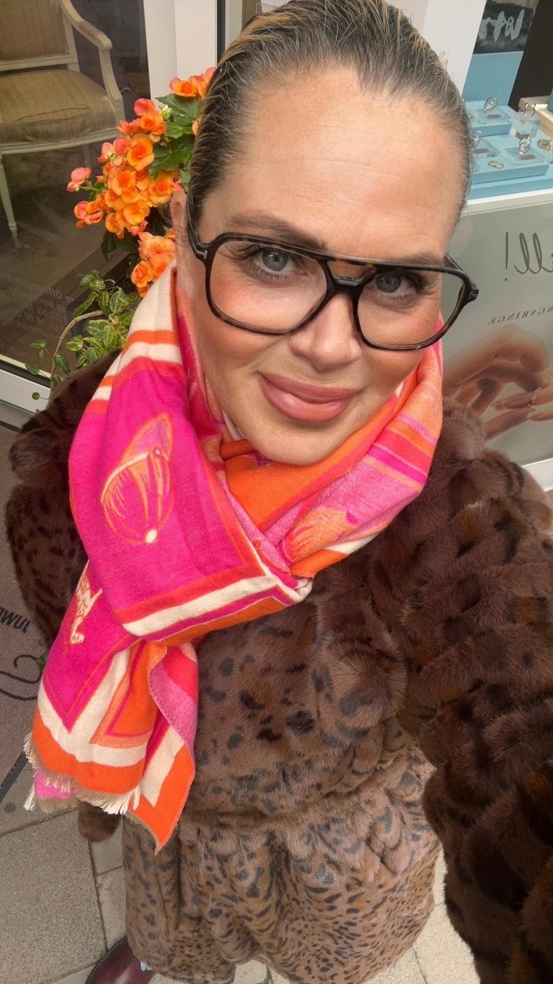 Frau trägt Leo Fake Fur Mantel in Braun, orange, pink, beigem Schal. Und große Brille.
