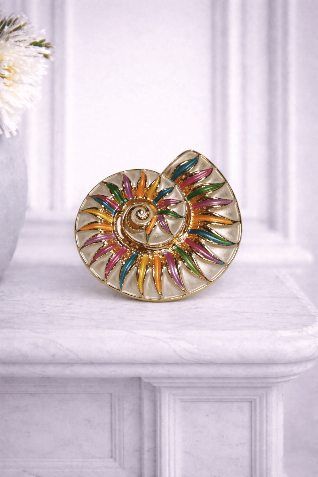 Goldfarbene Magnetbrosche in Spiralform mit emaillierten Details in Pink, Grün, Blau und Orange, fotografiert vor hellem Hintergrund.