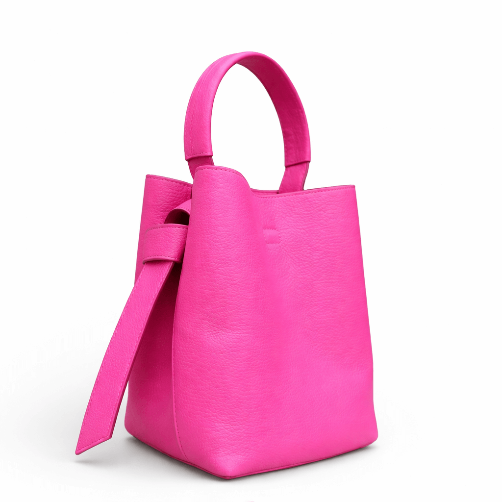 Pinke Handtasche aus strukturiertem Leder mit rundem Tragegriff und seitlichem Lederriemen, freigestellt vor weißem Hintergrund.